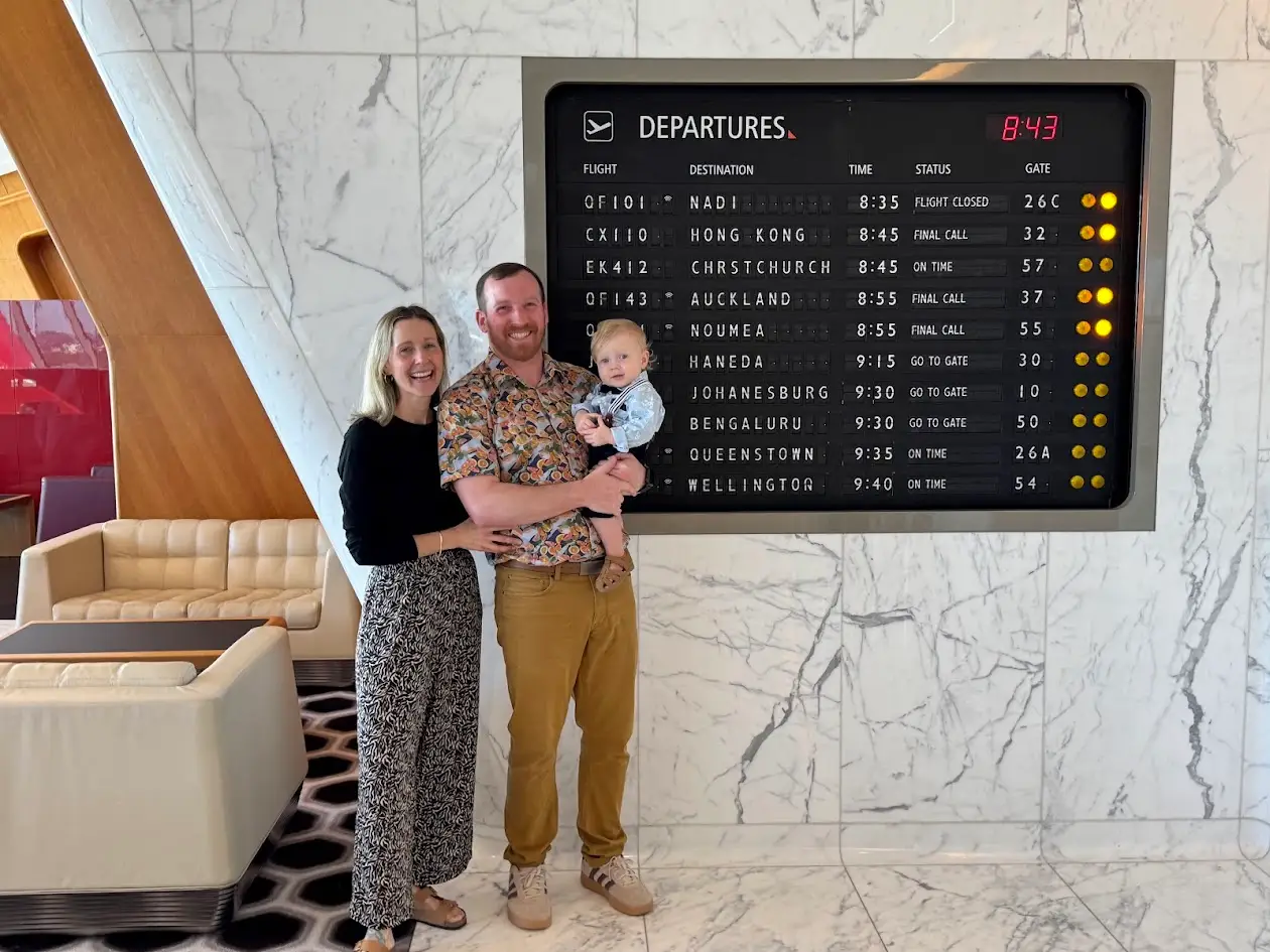 The author, his wife, and son in front of the old-timey departures flip board at the Qantas lounge.