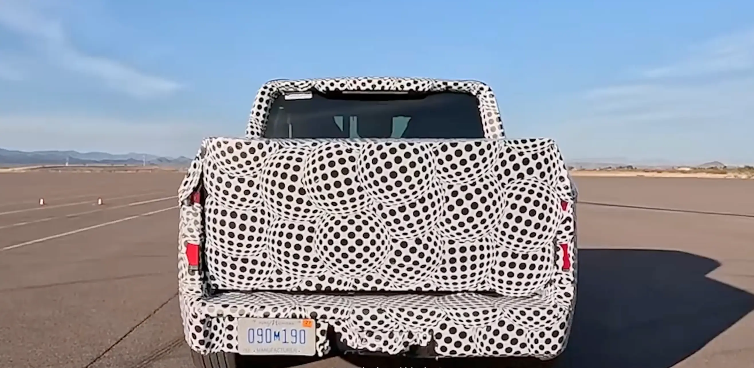 A camouflaged Ford EV pickup truck on a testing track.