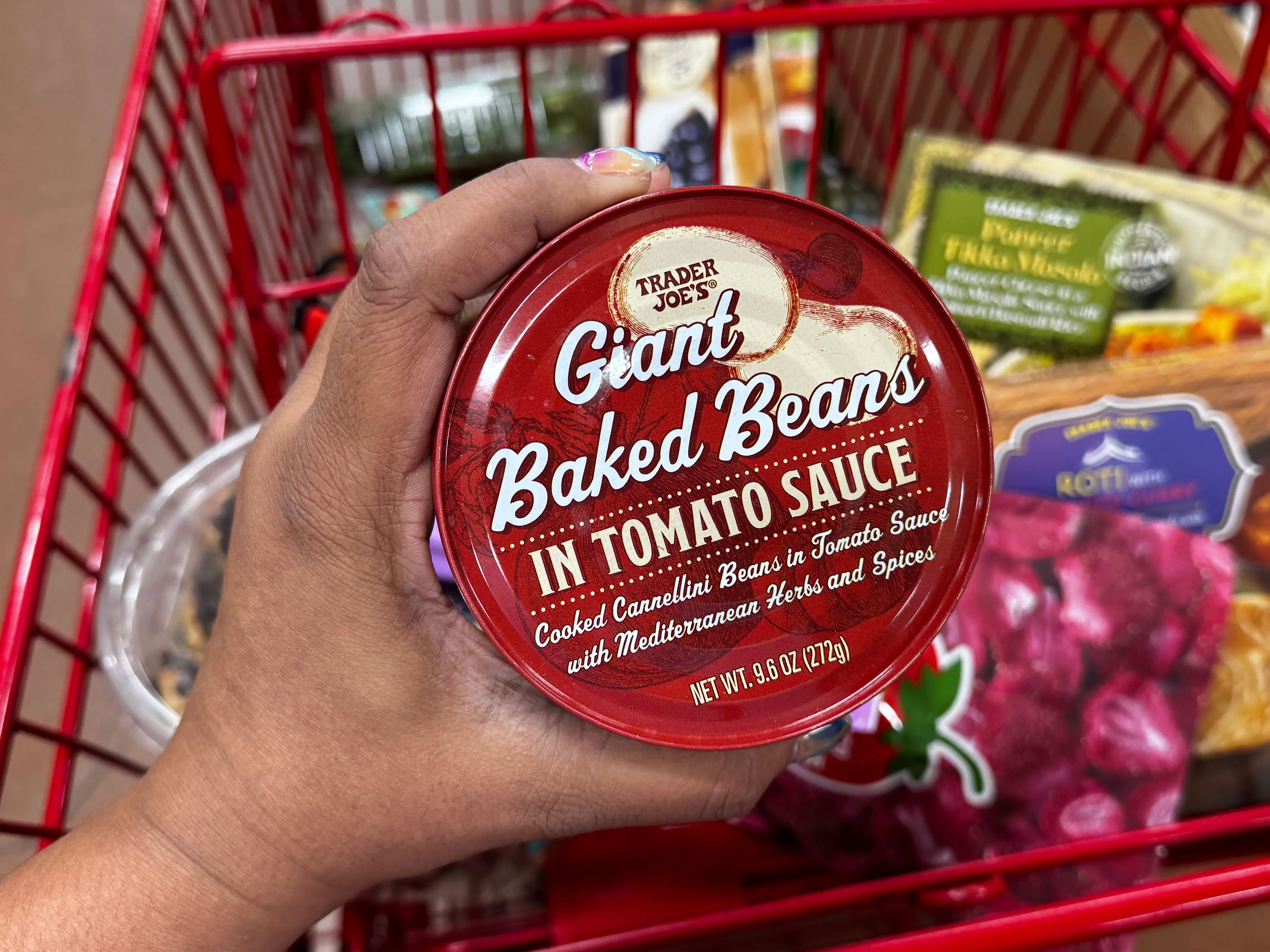 A hand holding a container of Trader Joe's giant baked beans in tomato sauce.