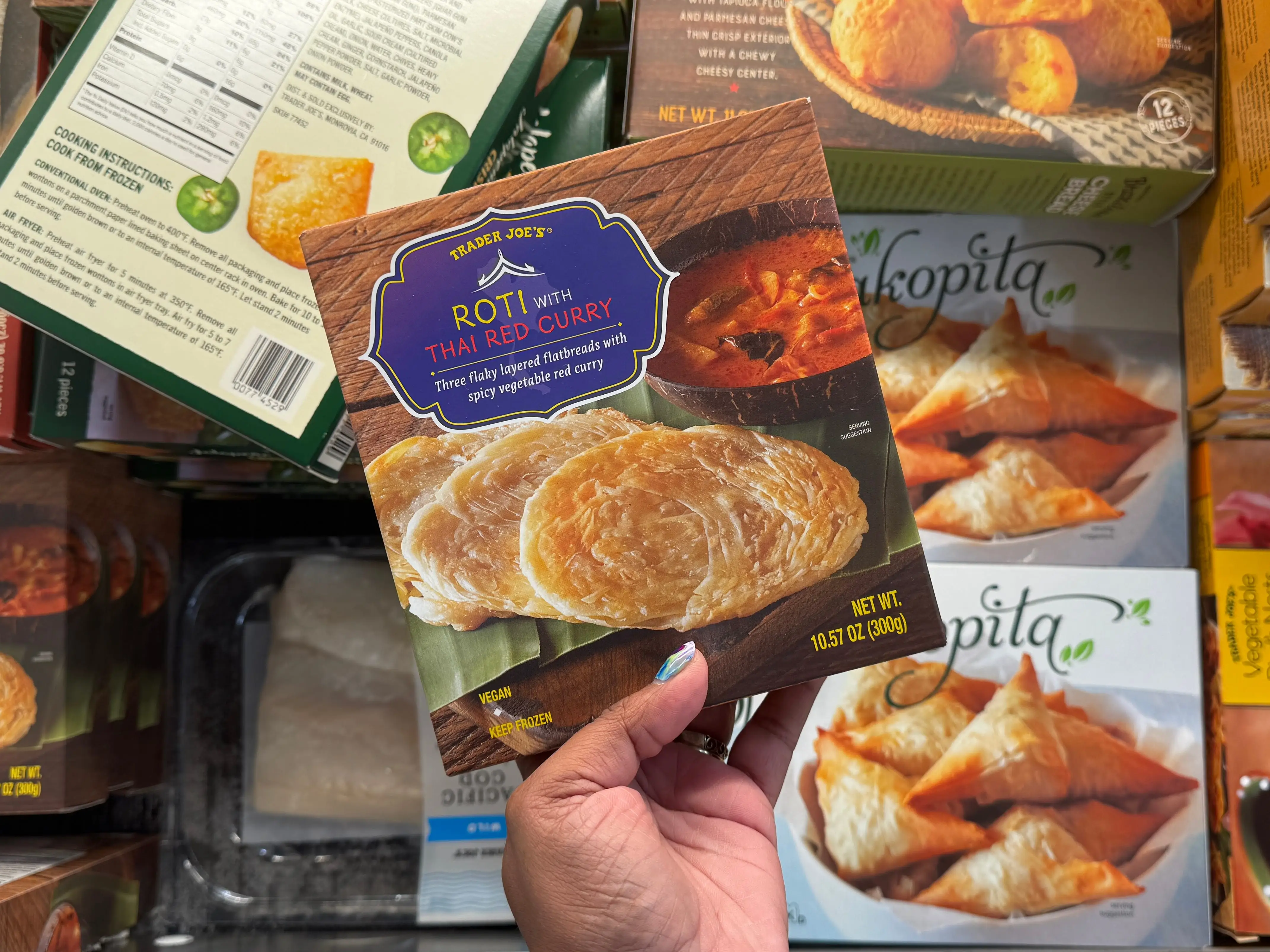 A hand holding a box of Trader Joe's Roti with Thai red curry.