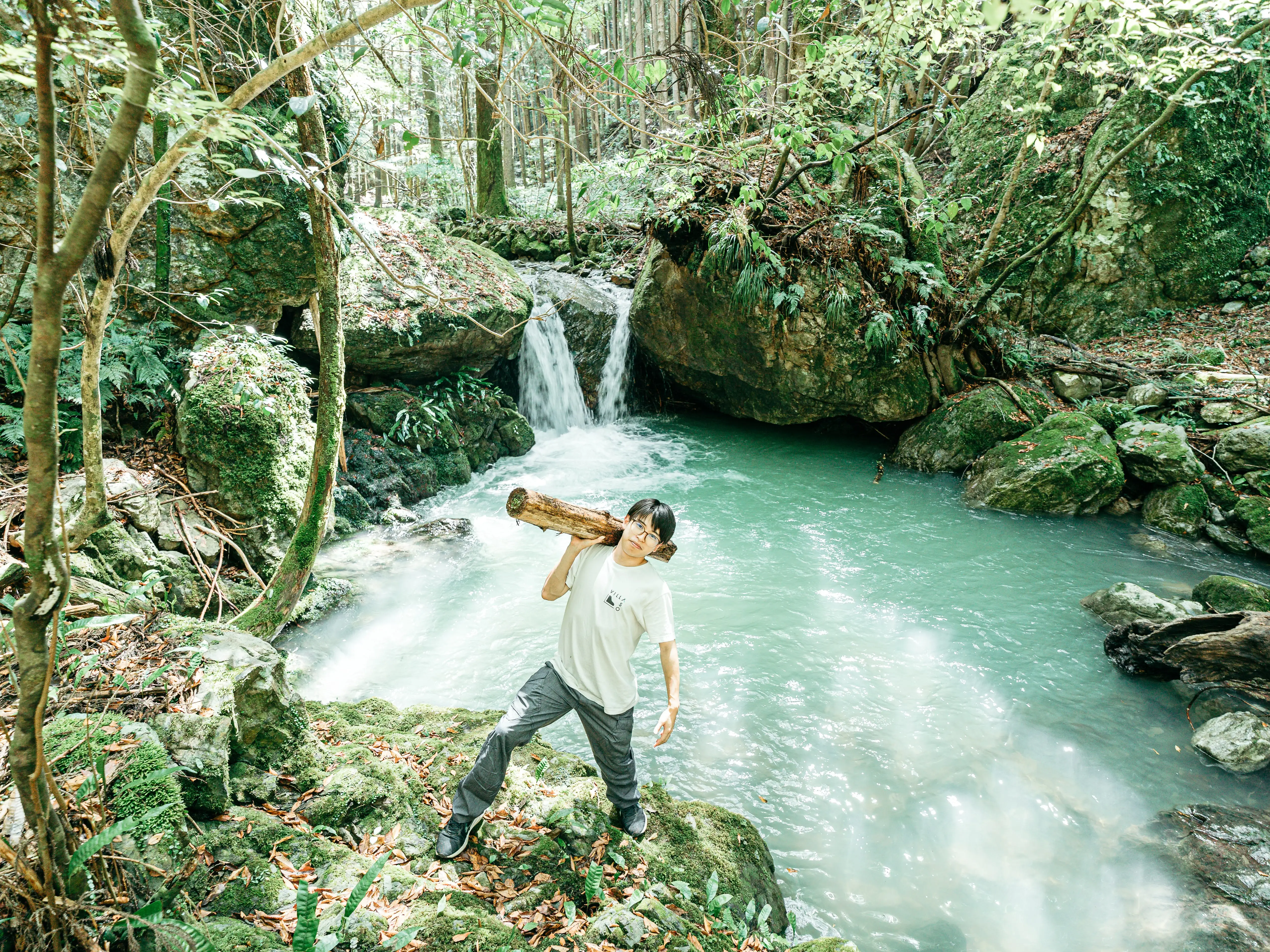 A man holding a piece of word with a waterfall in the background in Japan.