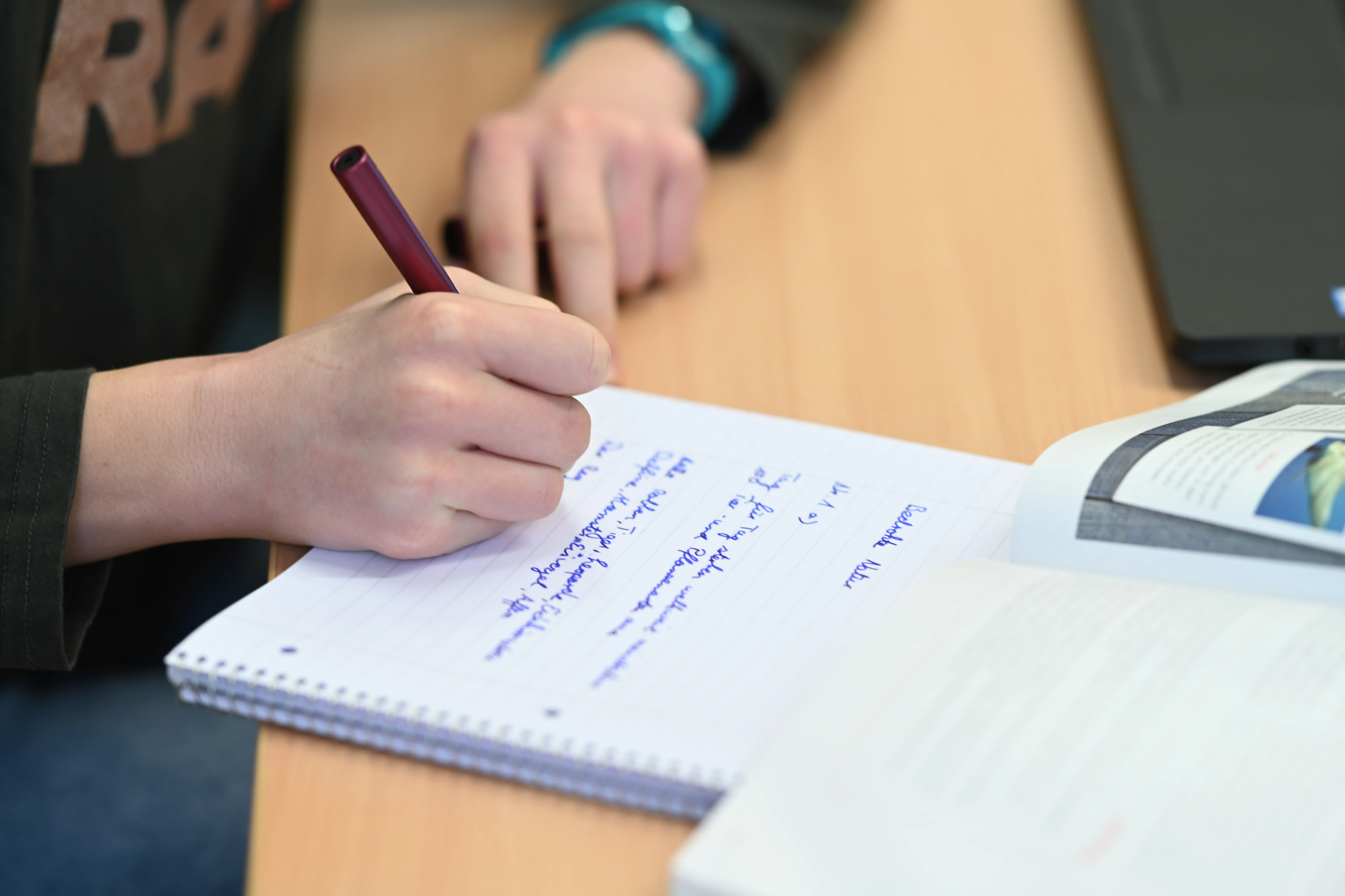 A student learns on her laptop while taking notes by hand.