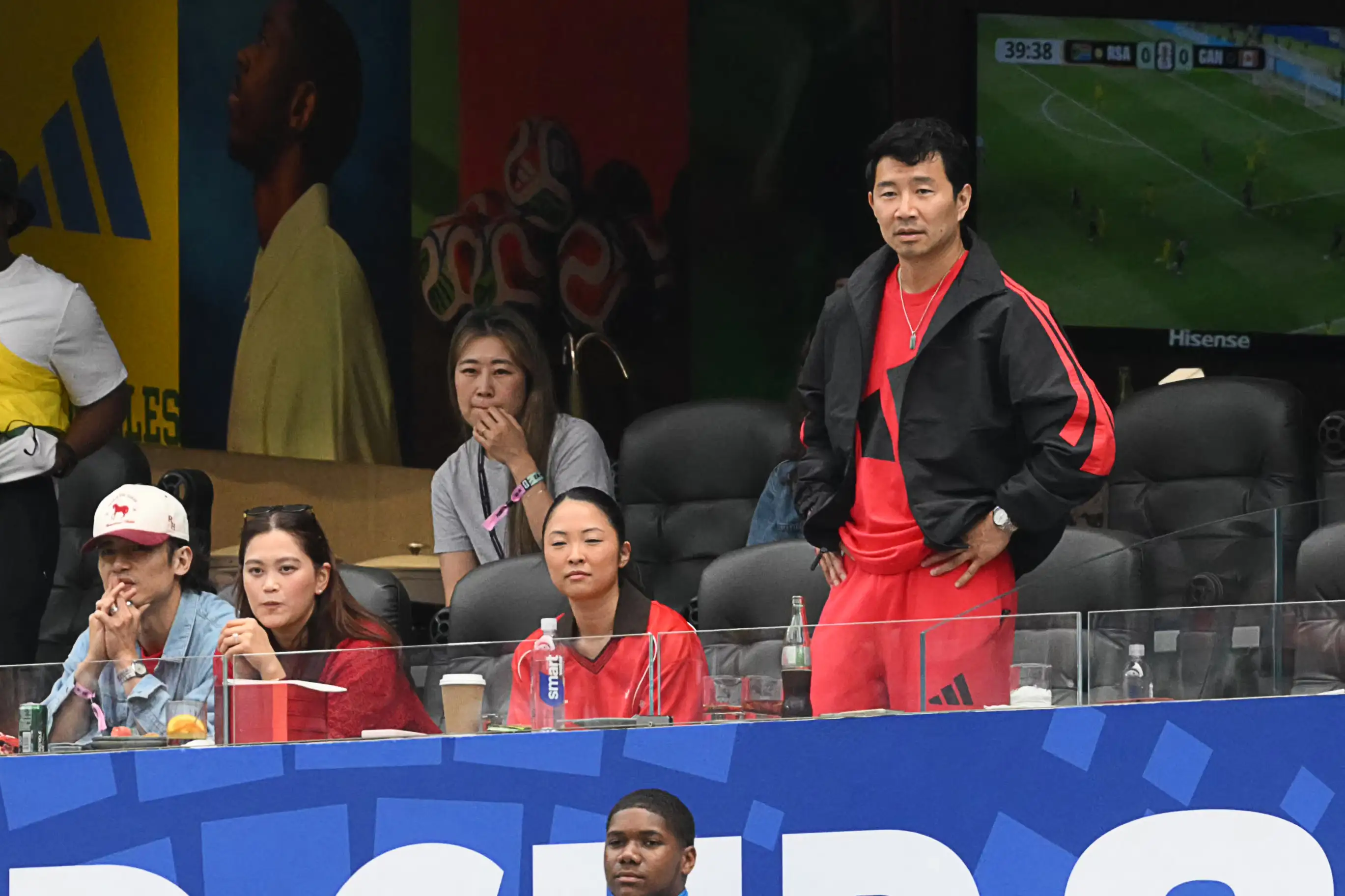 Canadian actor Simu Liu (R) and South Korean-Canadian filmmaker Maggie Kang (C-back) attend the 2026 World Cup round of 32 football match between South Africa and Canada at the Los Angeles Stadium in Inglewood on June 28, 2026.