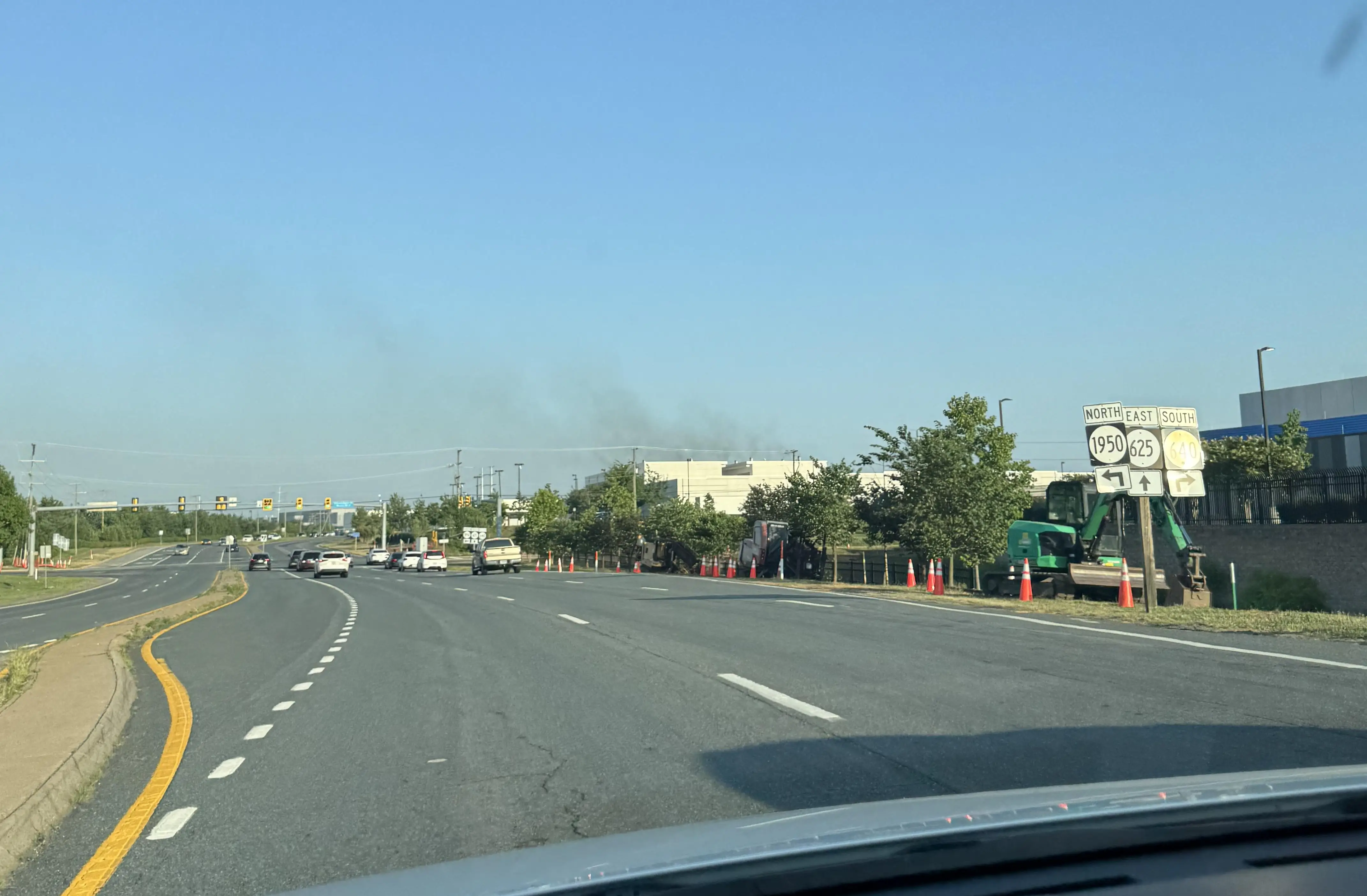 A photo shot from a vehicle driving down a wide roadway show smoke rising from a boxy white data center in the distance.