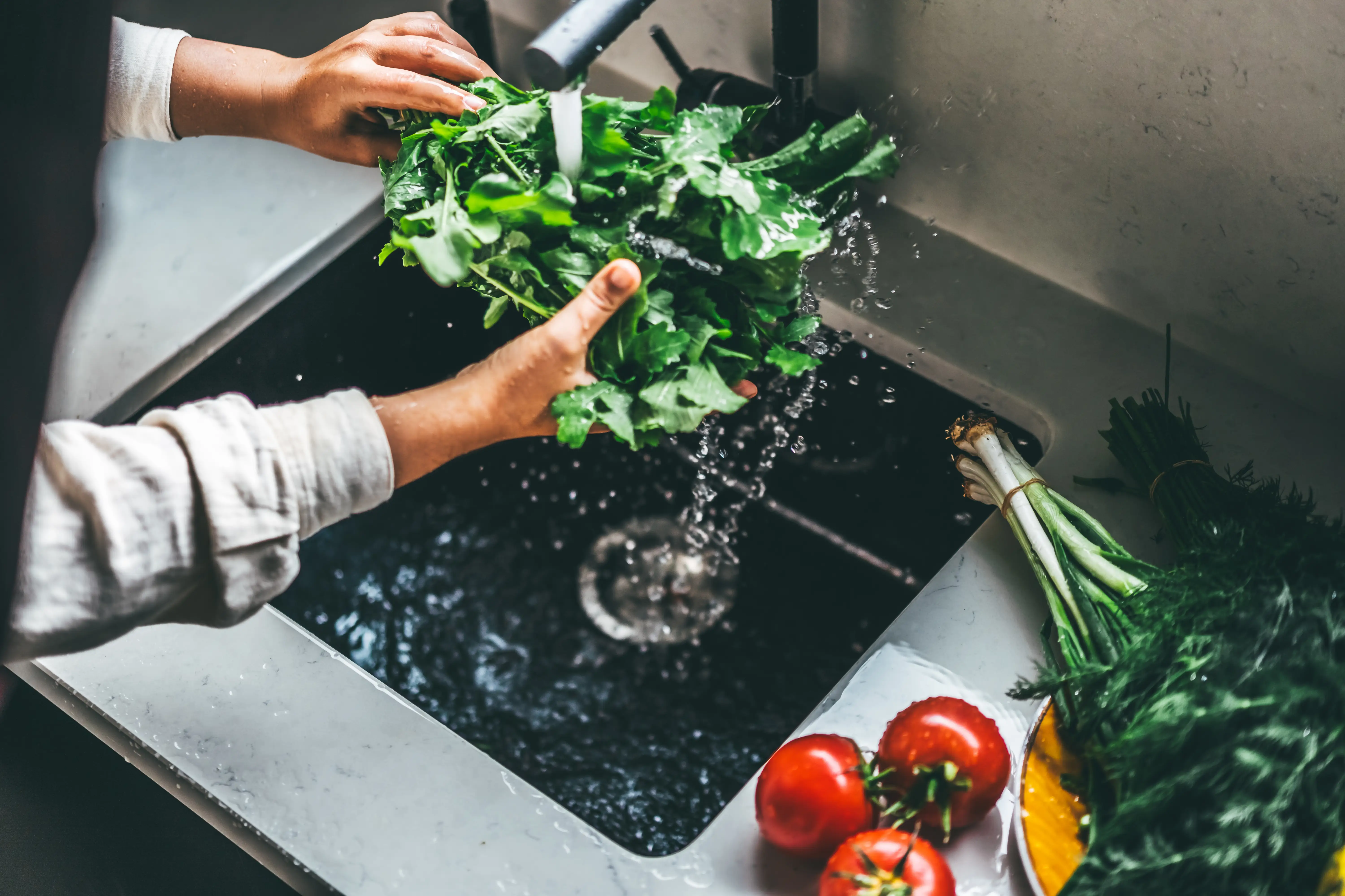 A person washes green leaves in their sink.