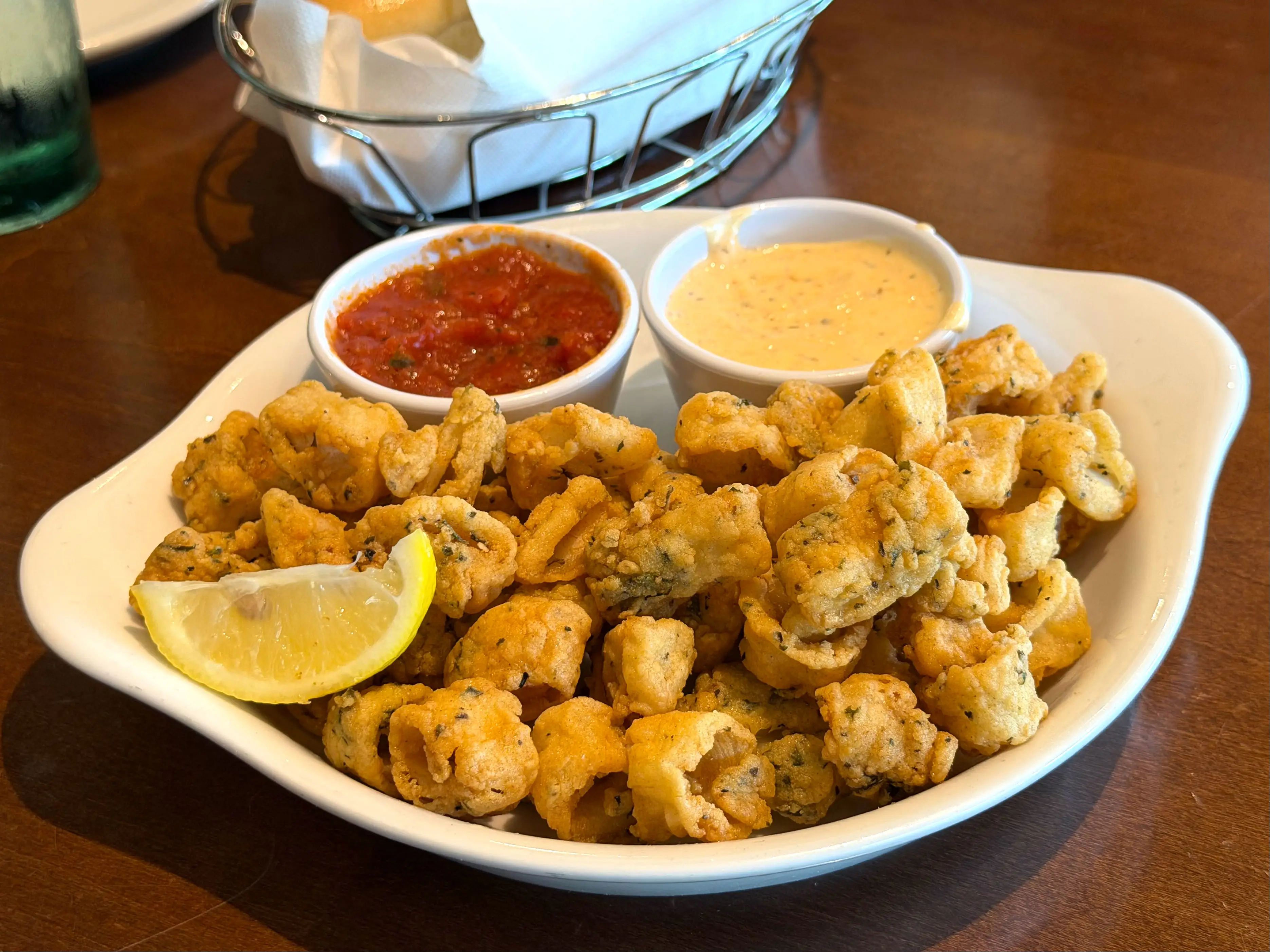 A plate of fried calamari with sides of marinara sauce and spicy ranch.