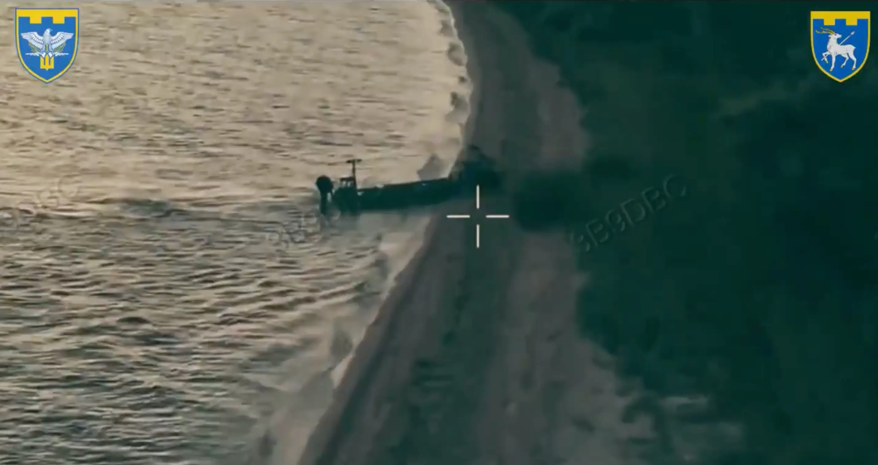 A naval drone parks against a beach. A ground robot rolls off the boat and onto the sand.