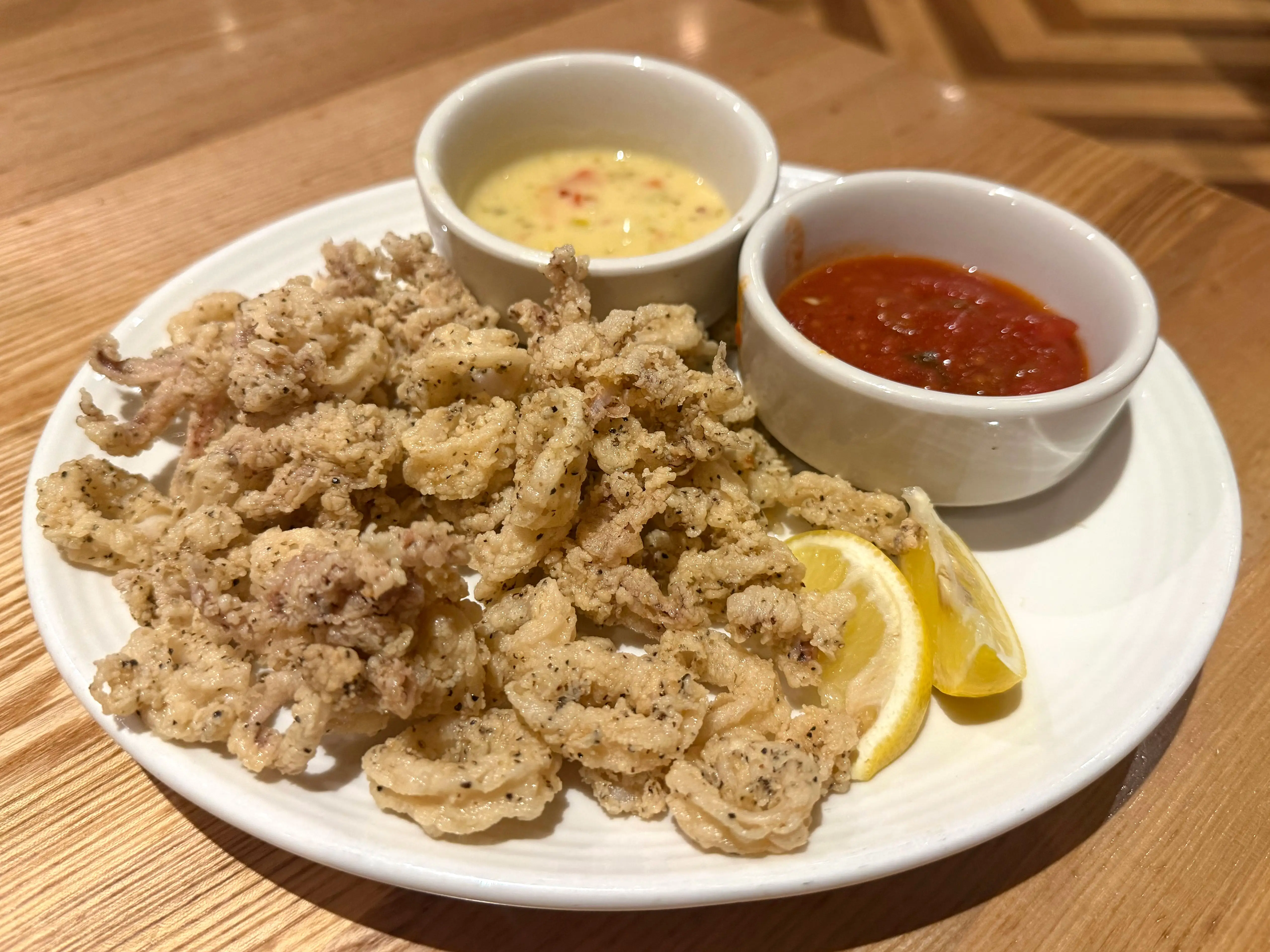 A plate of fried calamari with sides of marinara sauce and a lemon-butter sauce.