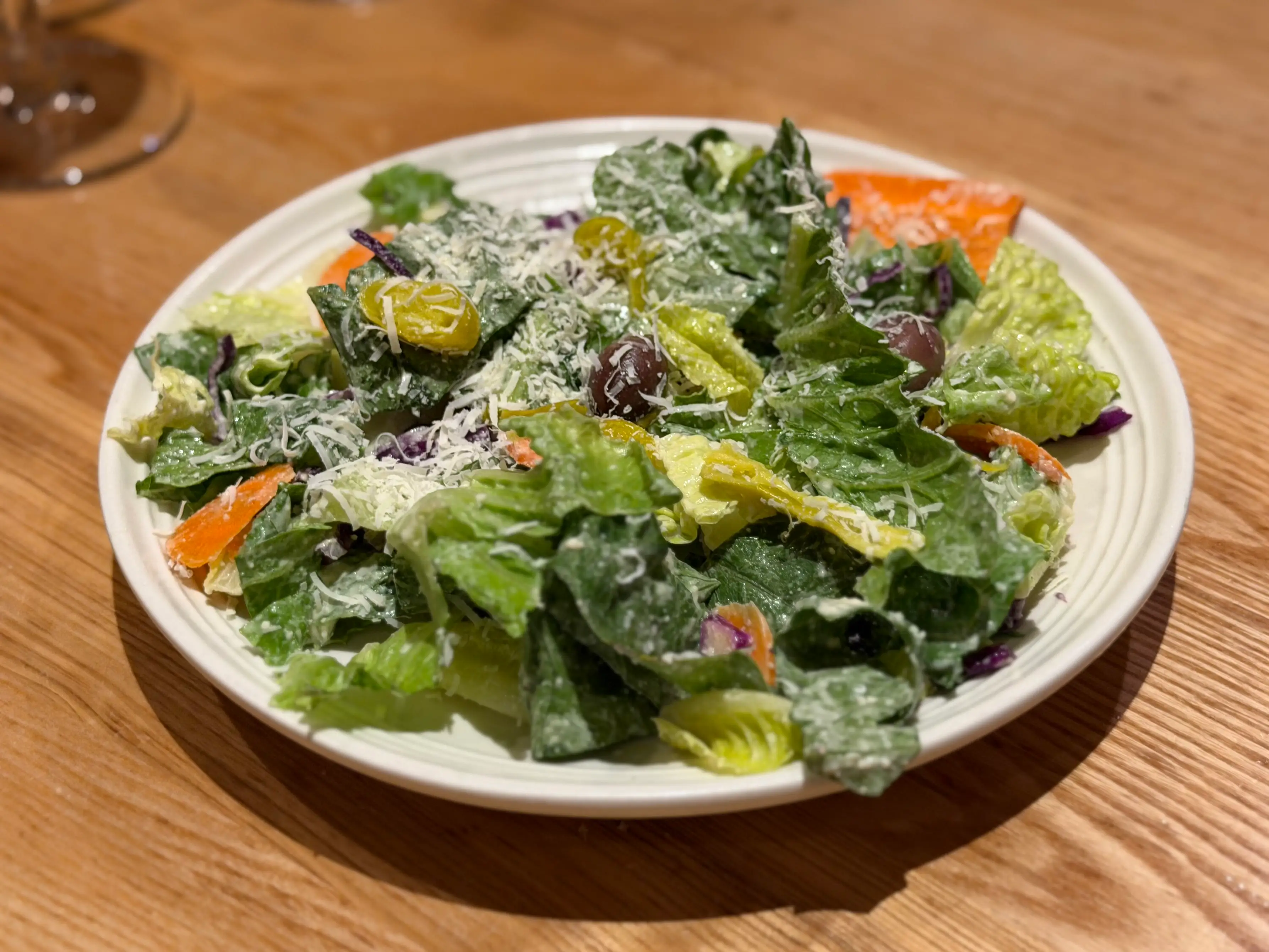 A plate of salad with lettuce, carrots, olives, and Parmesan cheese.
