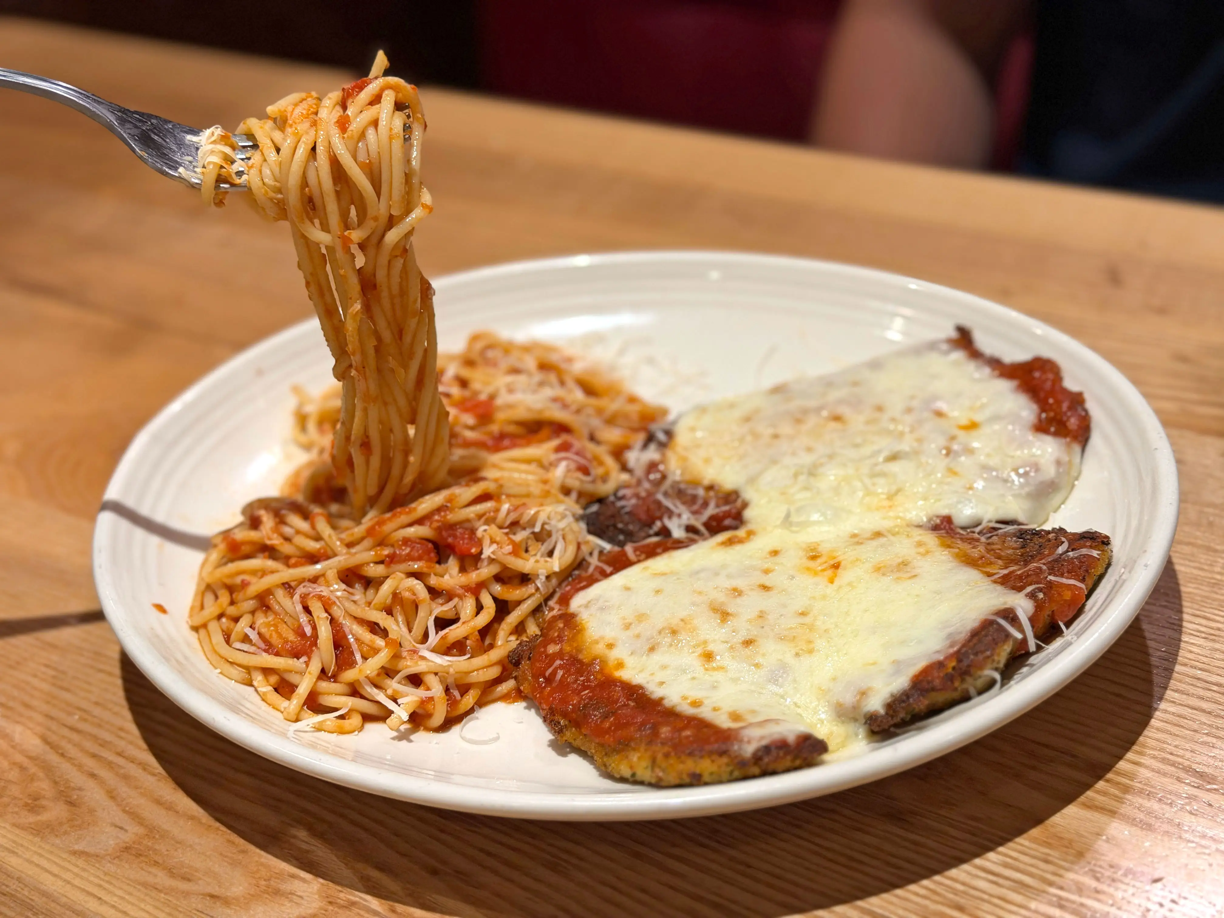 Two pieces of chicken Parmesan on a plate with spaghetti, some of which is being twirled on a fork.