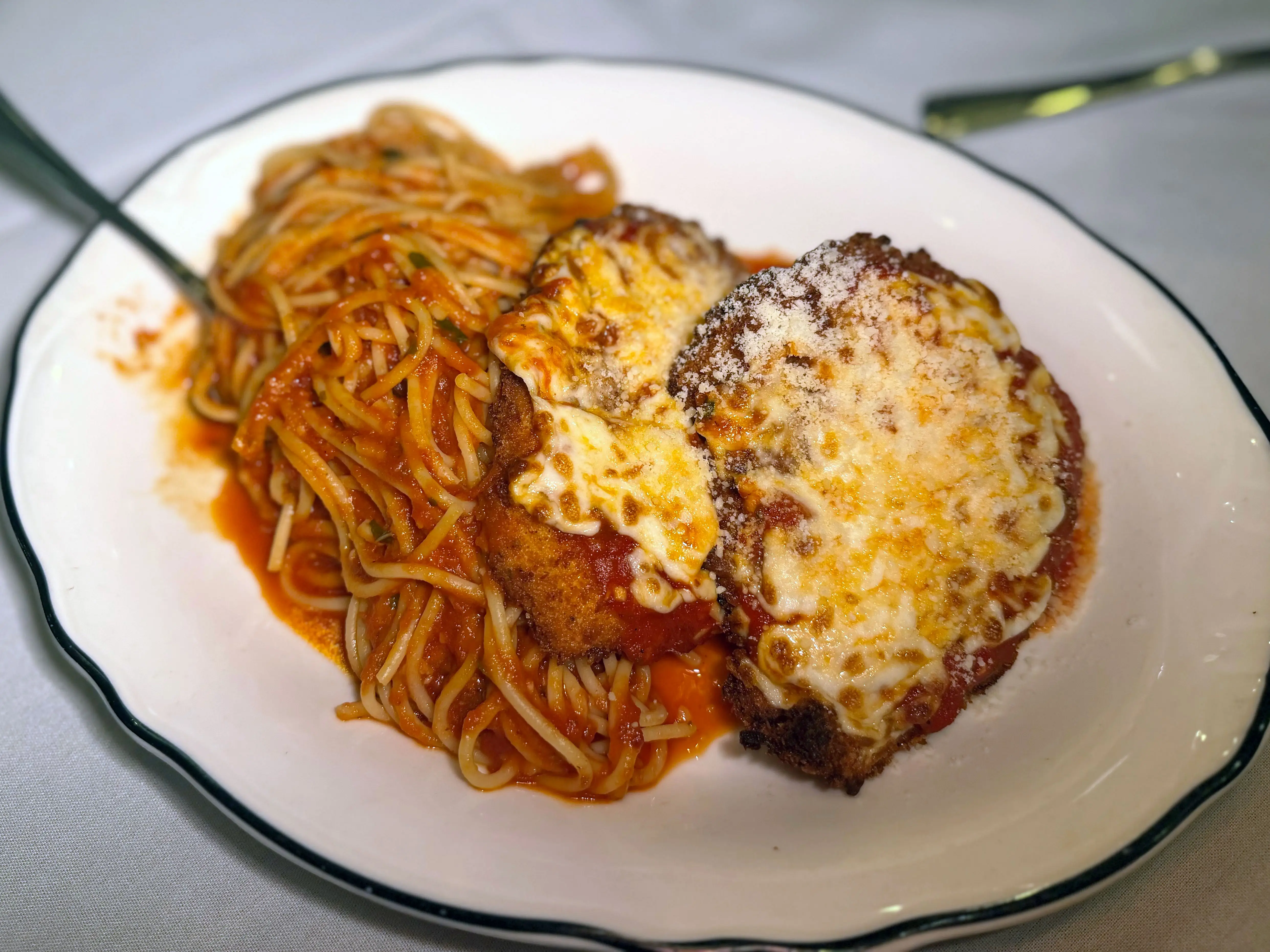 Two pieces of chicken Parmesan on a plate with spaghetti.