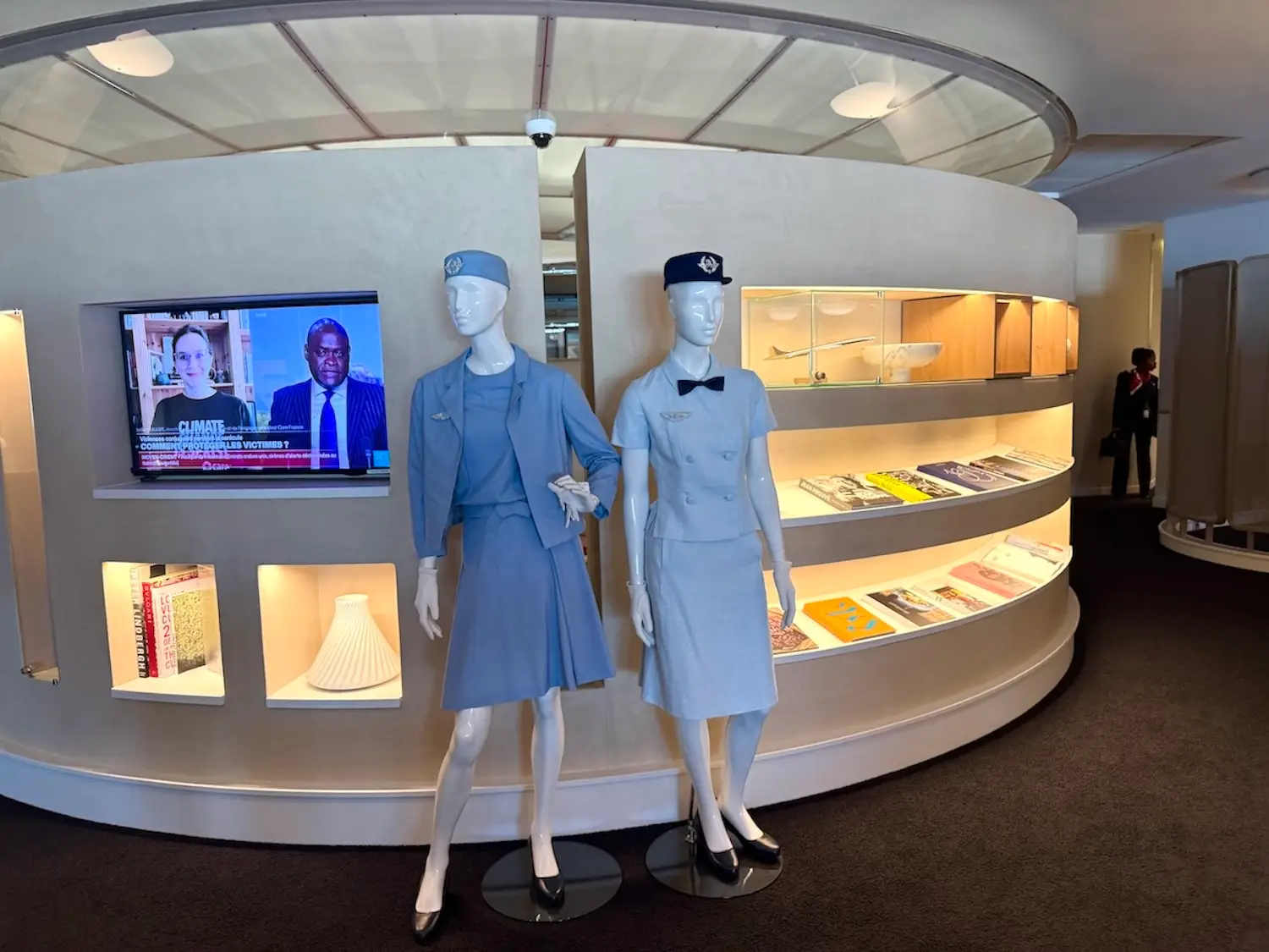 Two mannequins in flight attendant uniforms in front of backlit wall around CDG La Prèmiere lounge