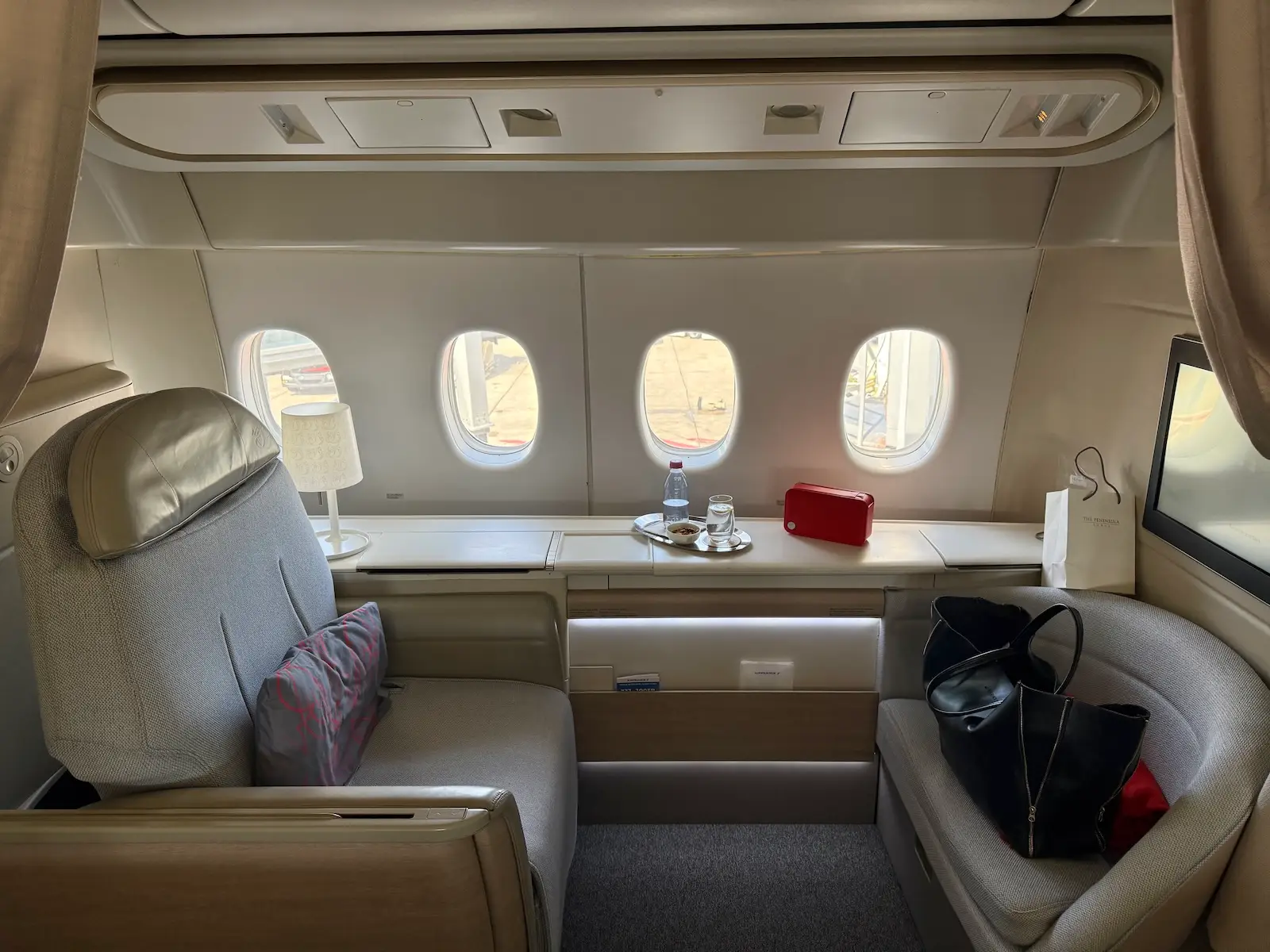 View of La Prèmiere Seat 1A with small footrest with bags on it, long ledge beside windows next to seat