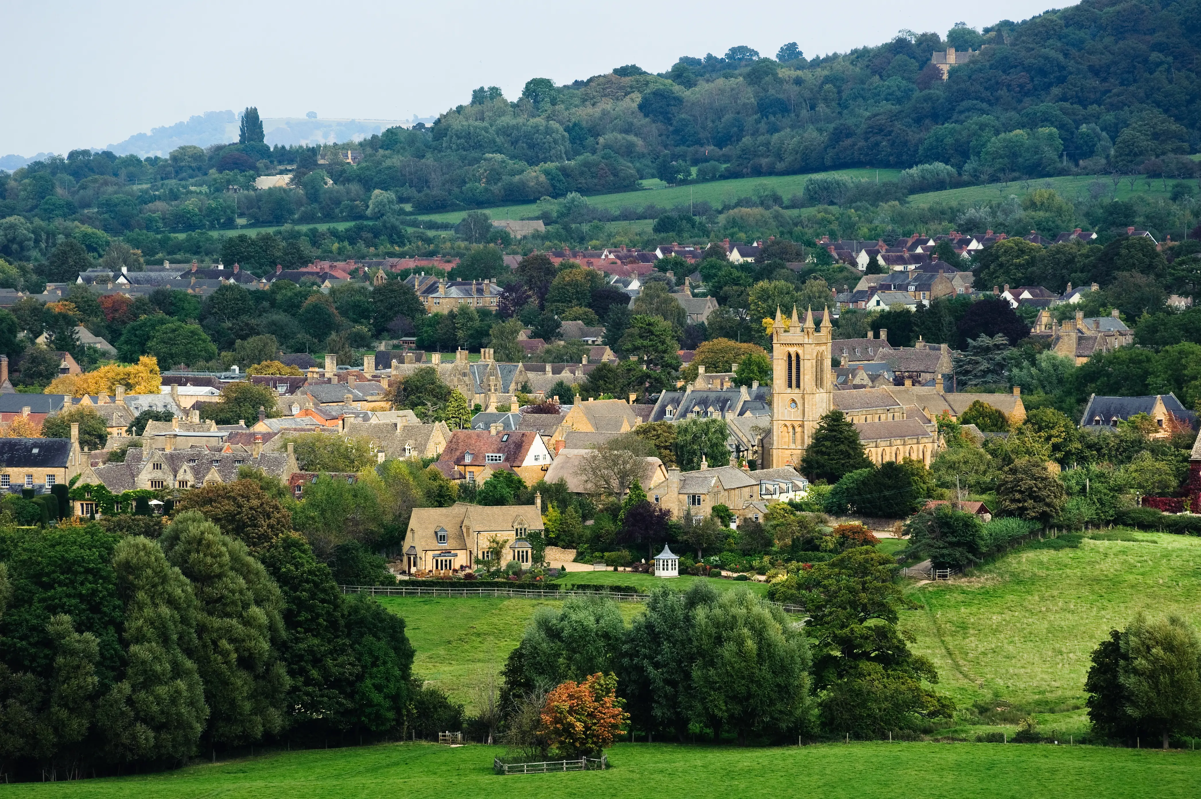 Stone village with a church tower sits among trees and green hills in a rural landscape.