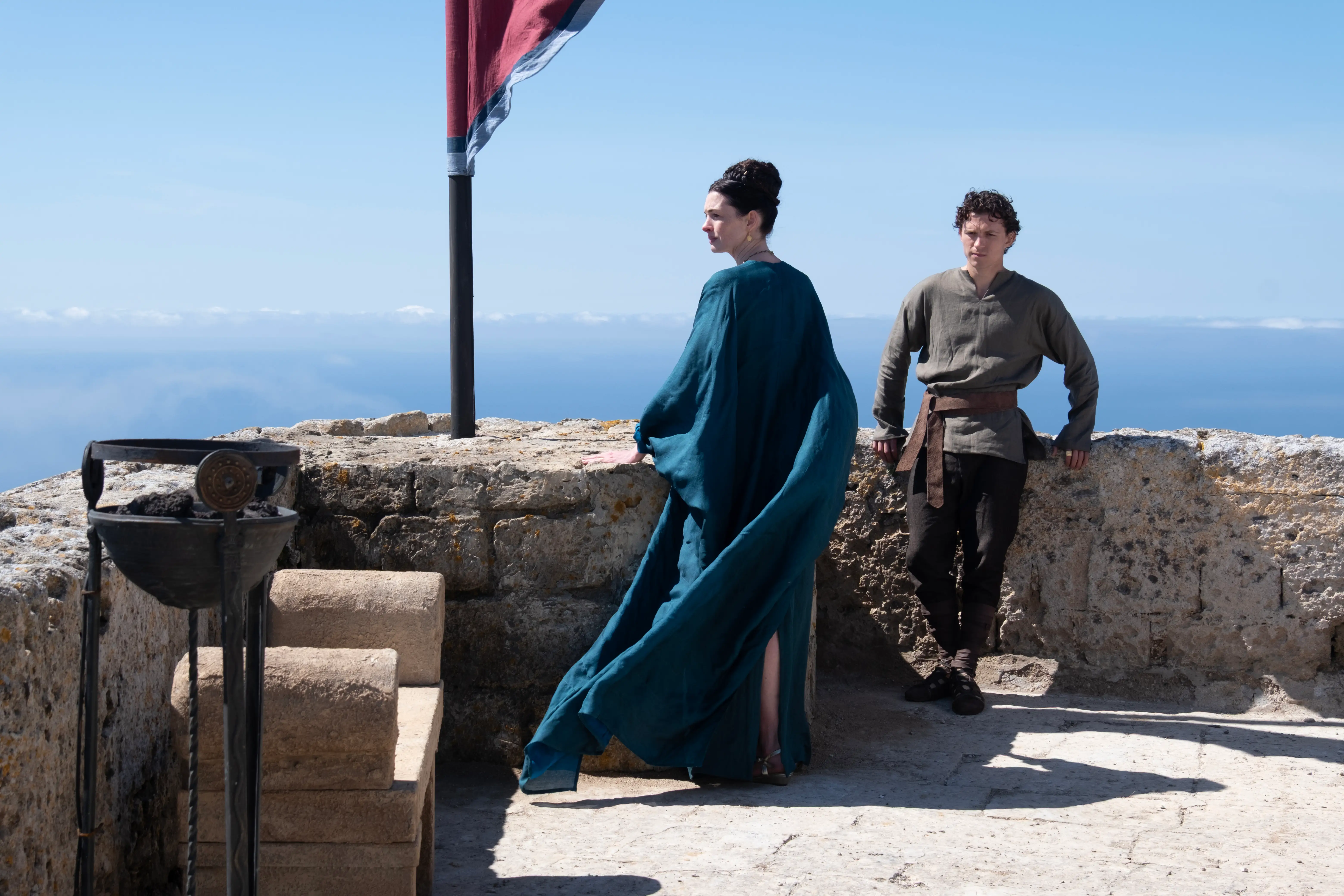 Anne Hathaway and Tom Holland standing by a stone wall in The Odyssey movie