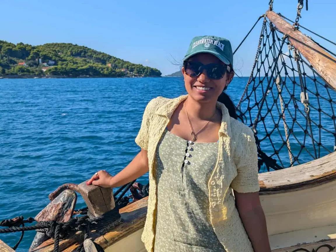 The writer wearing a dress and a hat, standing on a boat in front of the sea in Croatia.