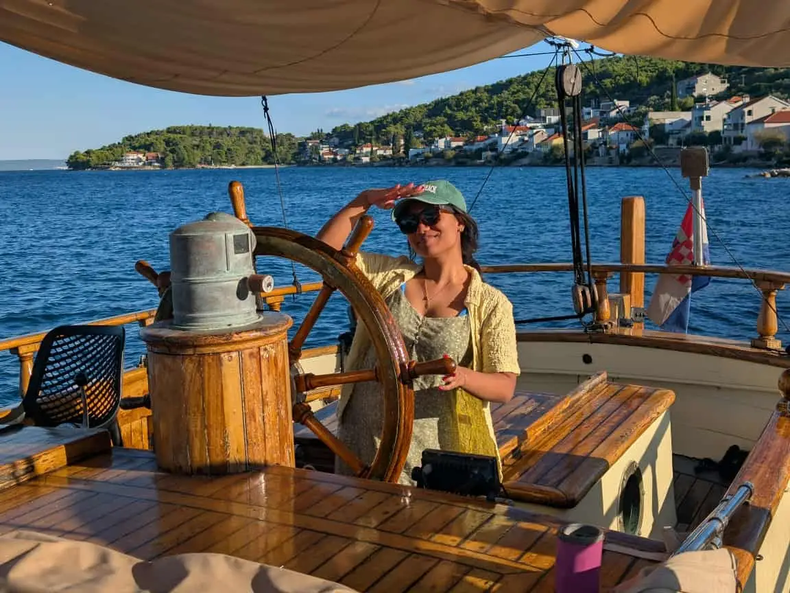 The writer steering a wheel on a boat in Croatia, with the water in the background.