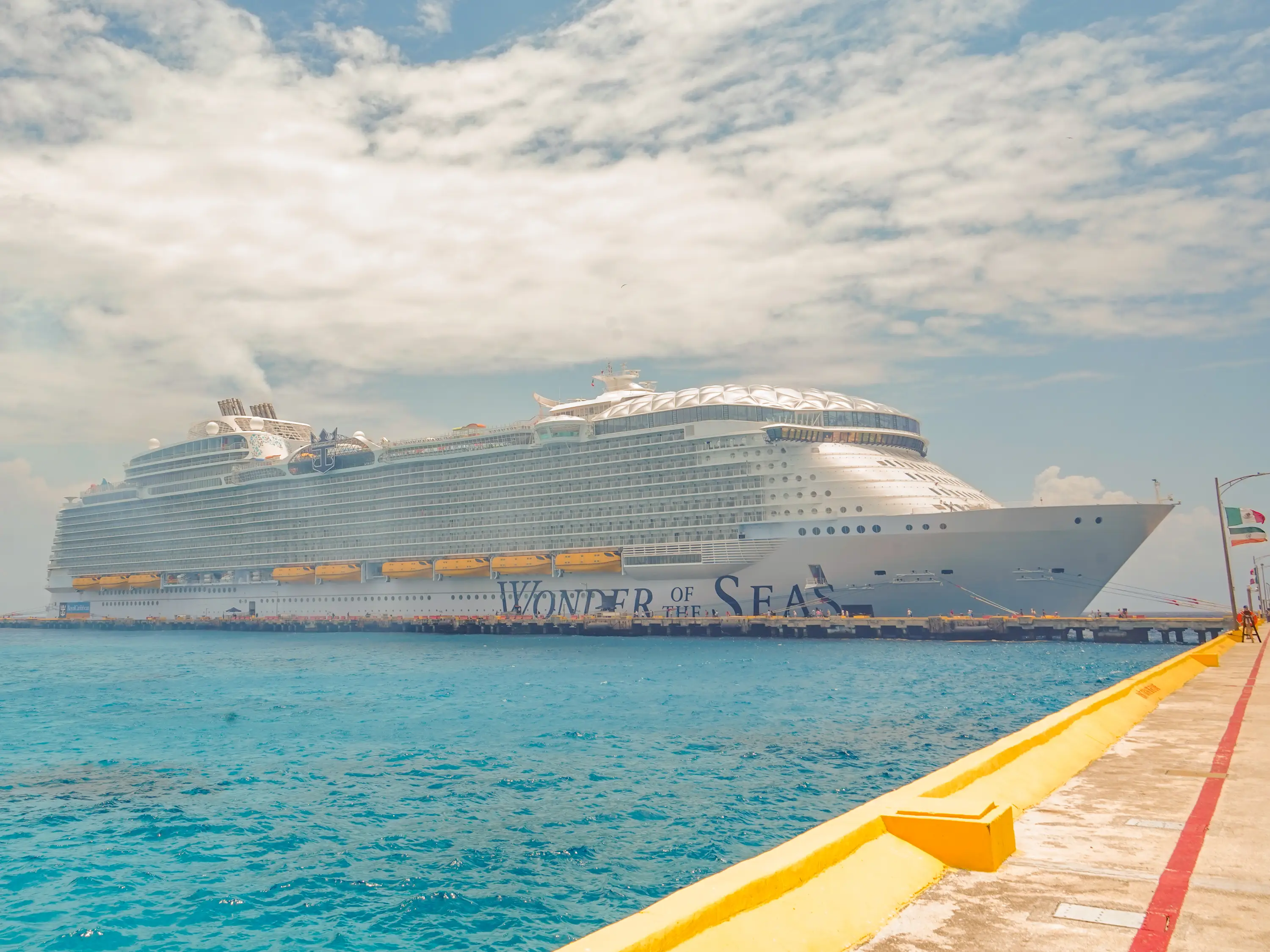 Cruise ship Wonder of the Seas docked beside turquoise water under a partly cloudy sky.