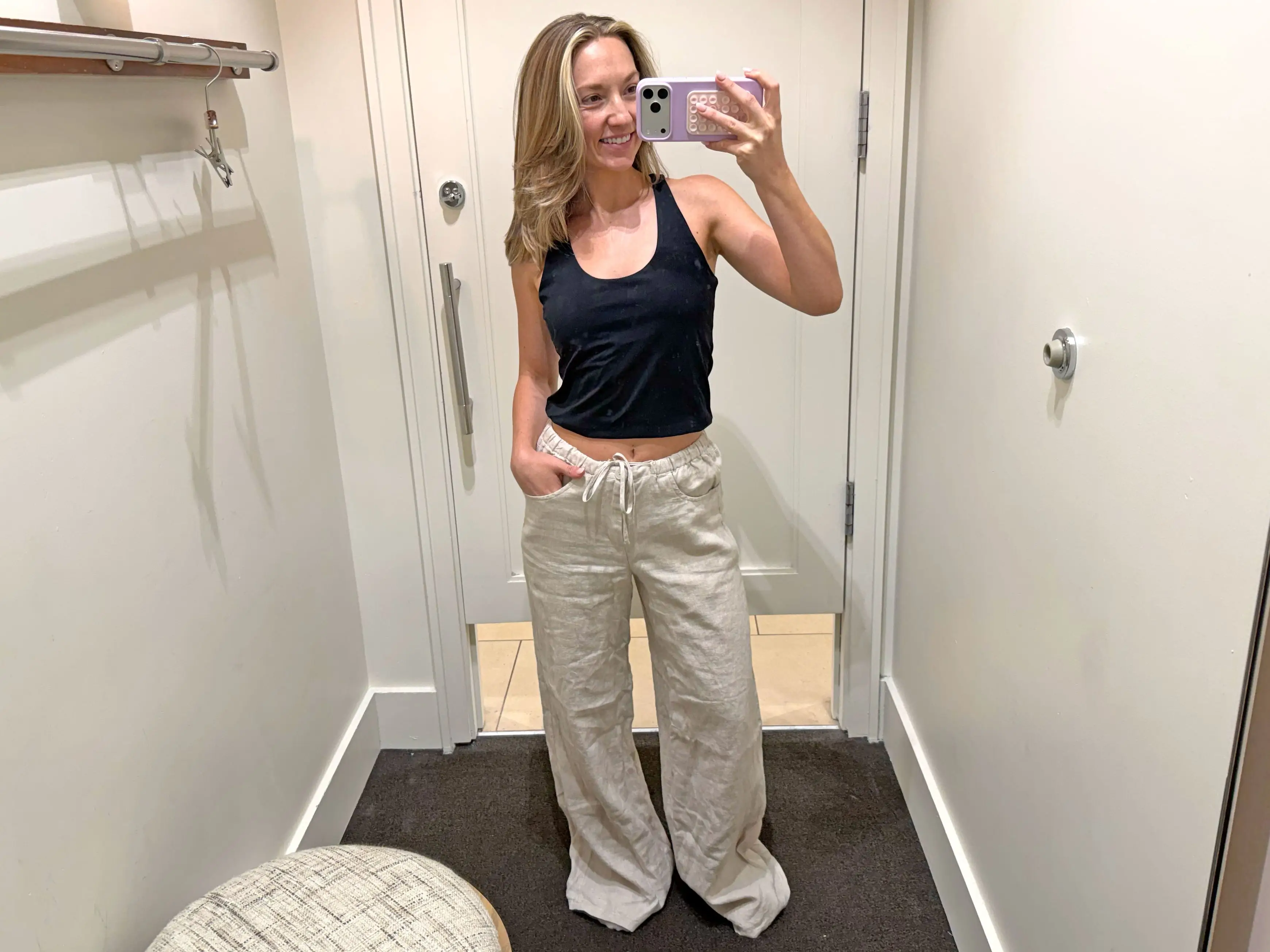 Chloe wears a pair of beige linen pants in a fitting room.
