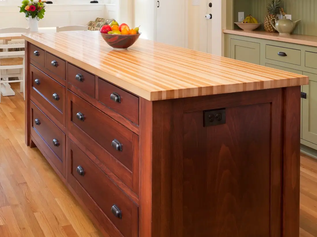 A kitchen with a butcher-block topped center island and black countertops.
