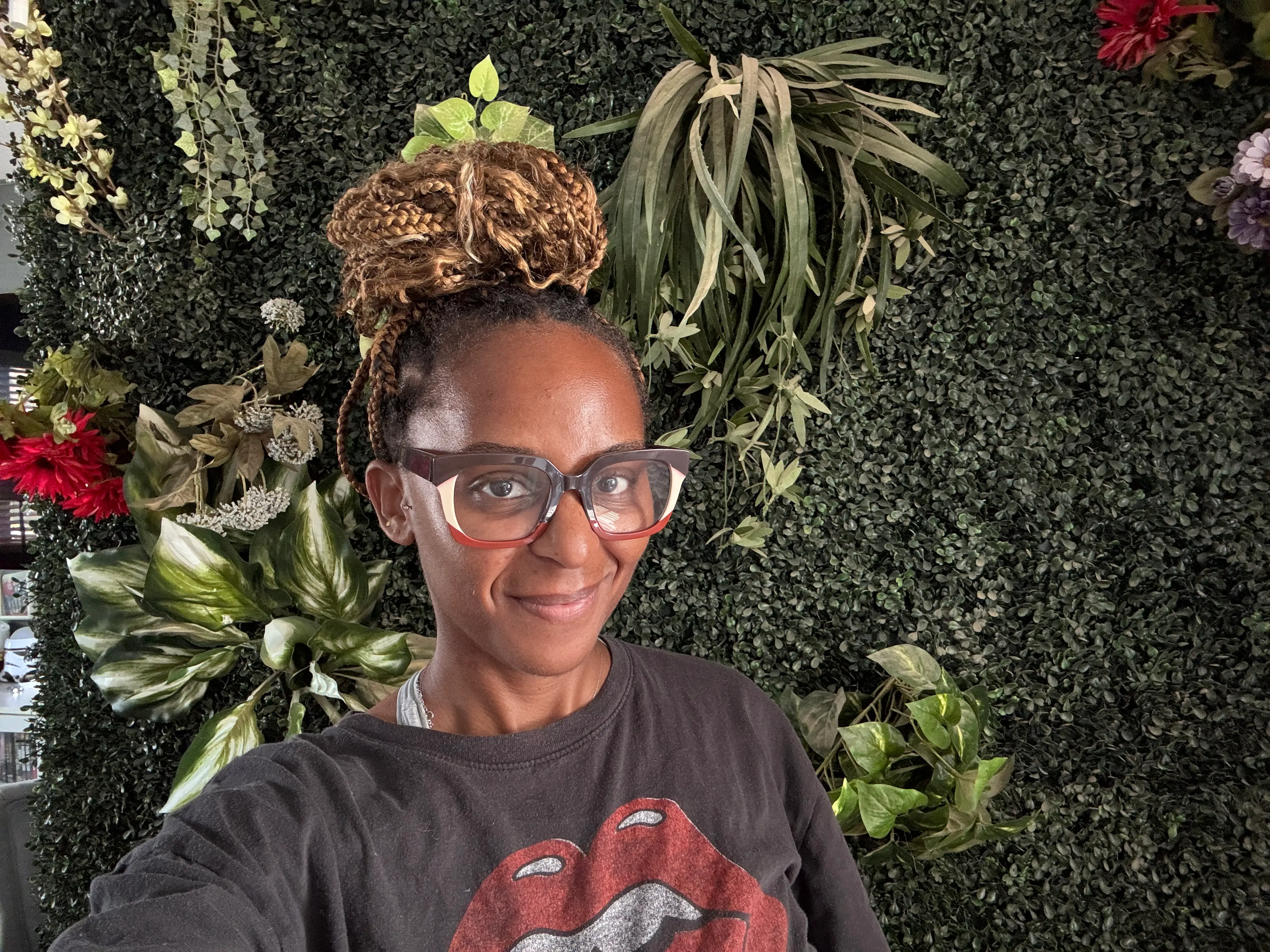 Woman with glasses smiling in front of greenery wall