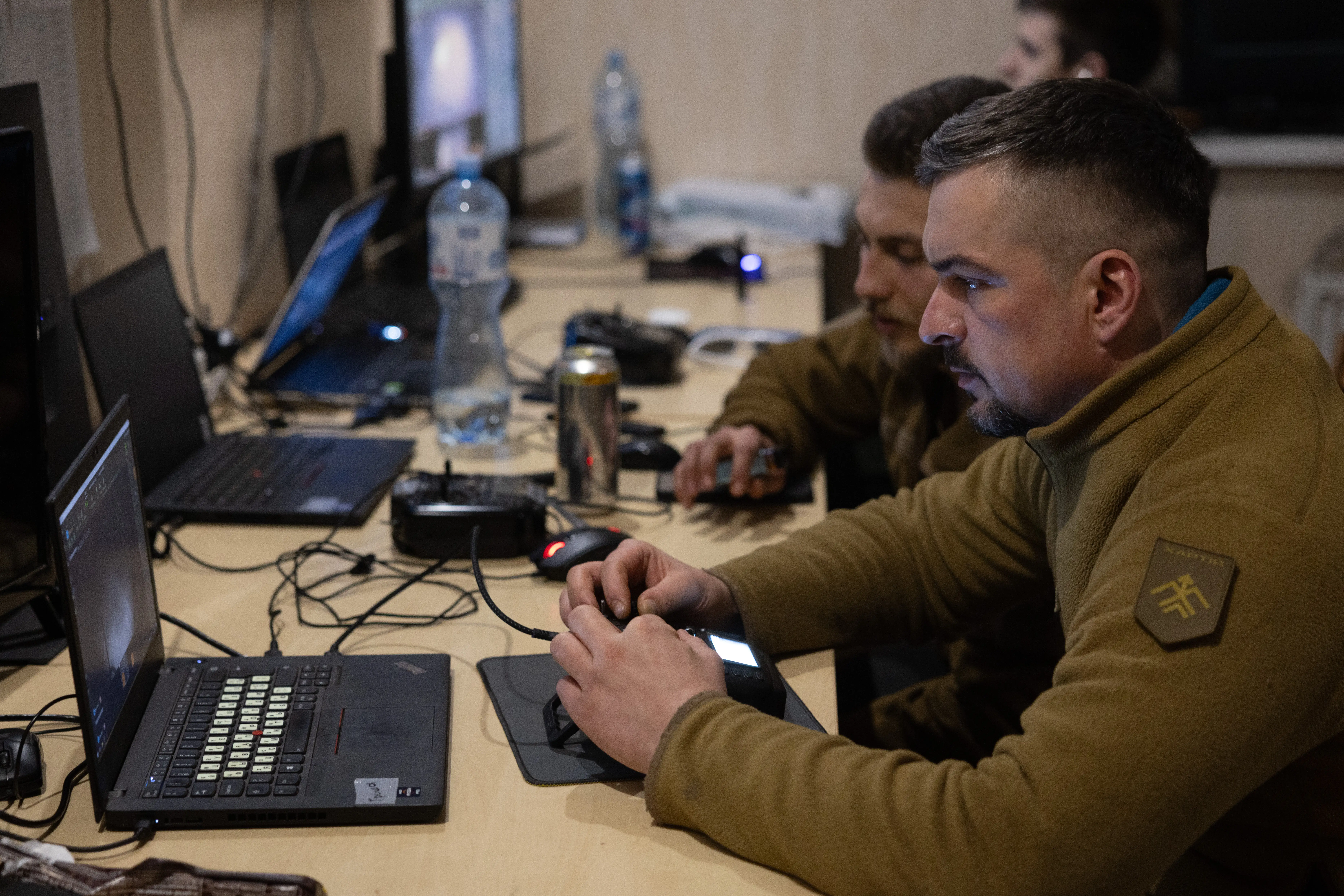 Men in khaki fleeces look at black laptops in a wood-lined room