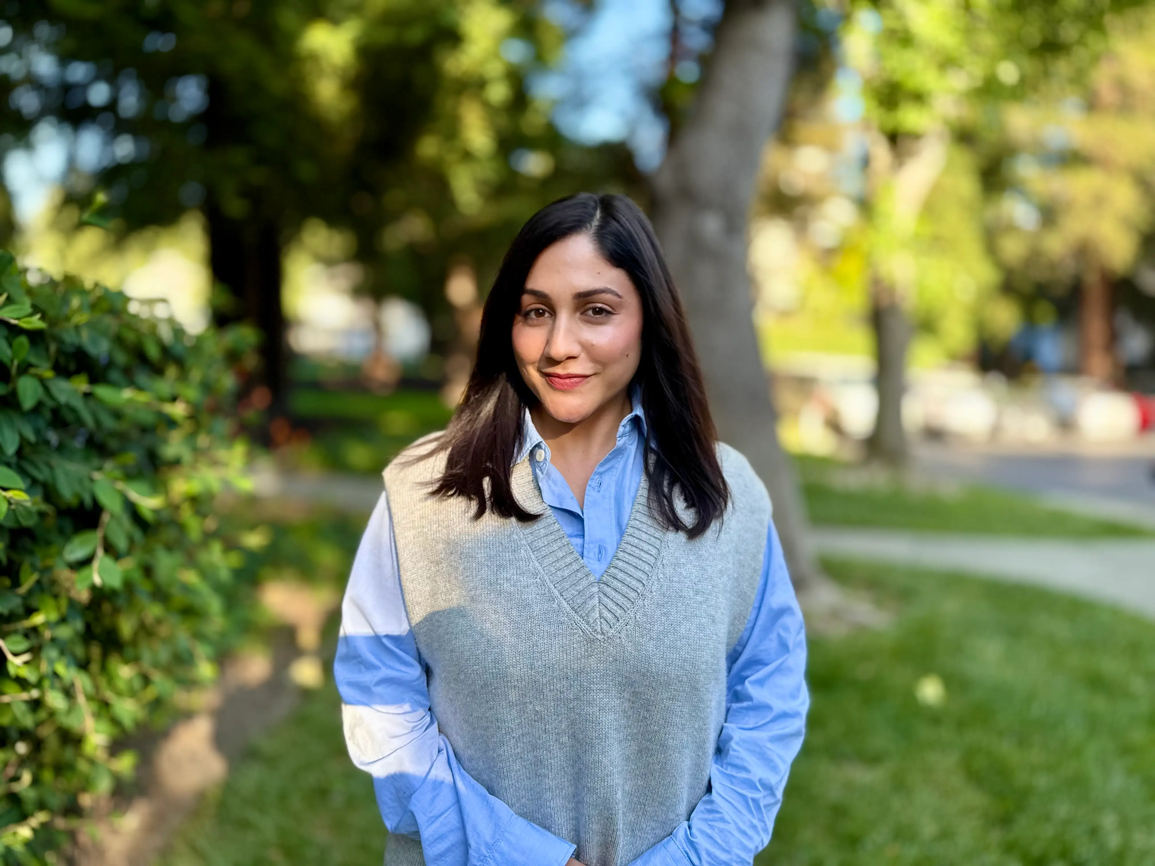 The author stands outside while wearing a blue shirt and gray vest.