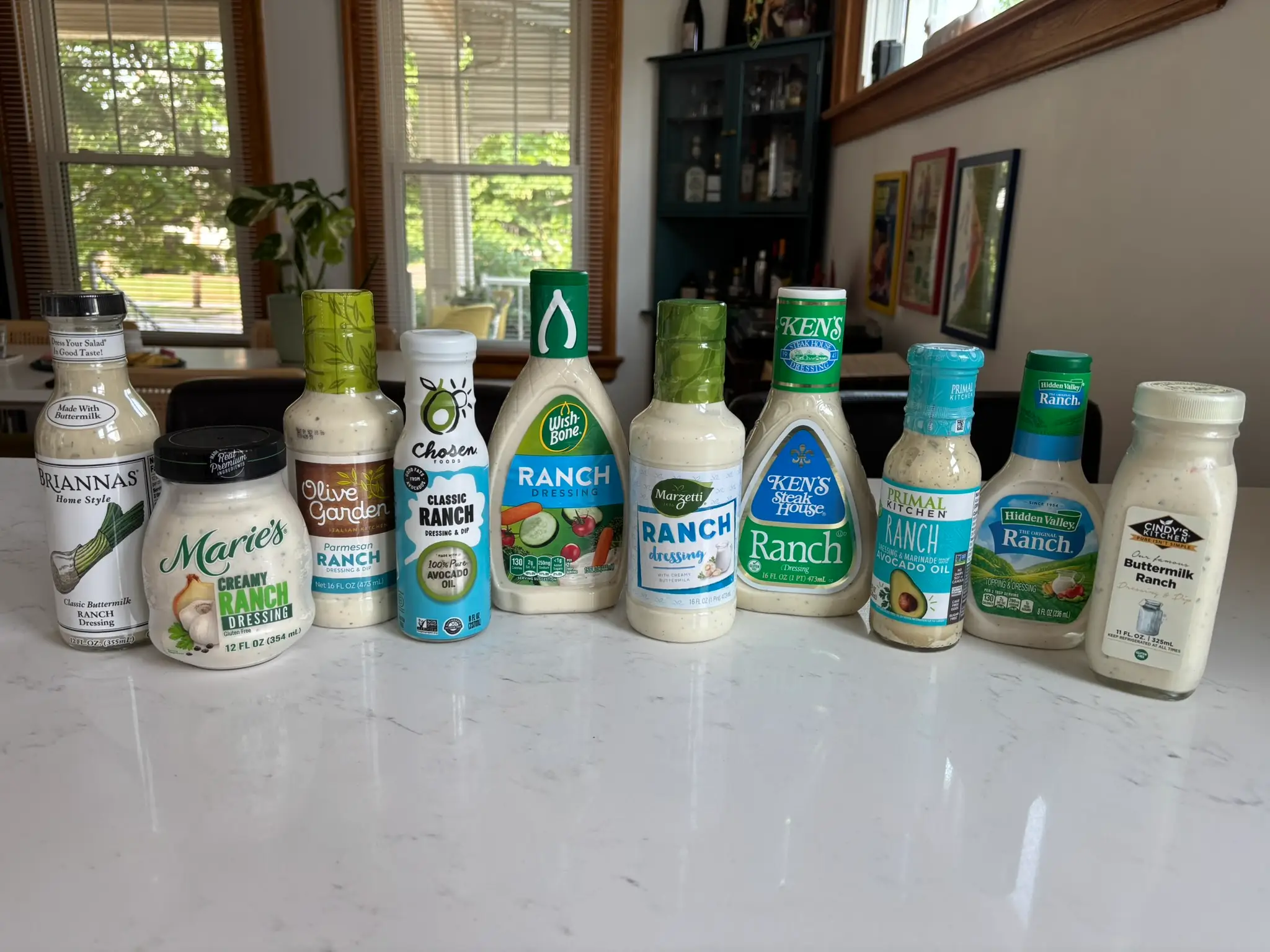 Bottles of ranch dressing on counter from Brianna's, Marie's, Olive Garden, Chosen Foods, Wish Bone, Marzetti, Ken's Steakhouse, Primal Kitchen, Hidden Valley, and Cindy's Kitchen.
