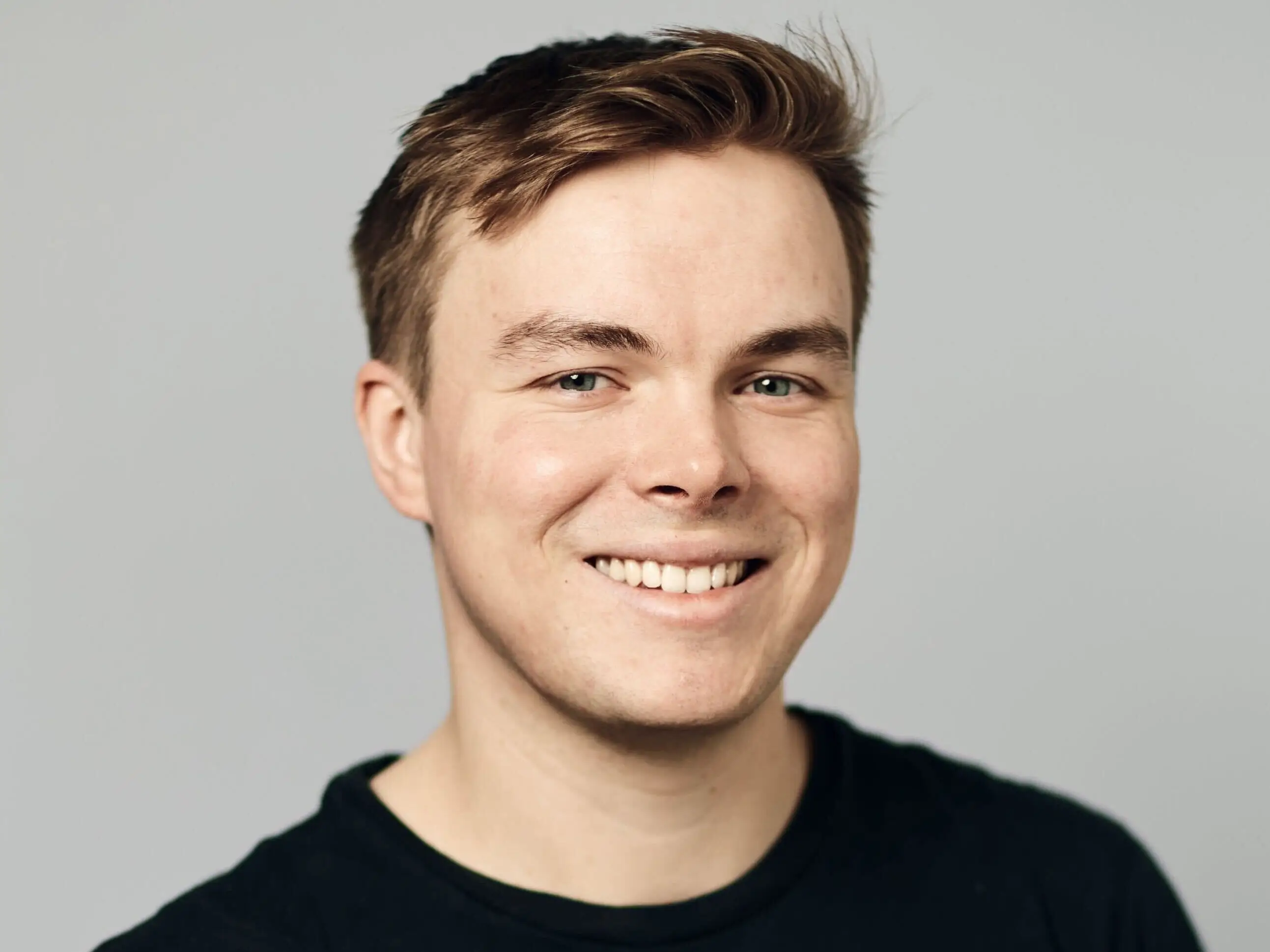Smiling man in a black shirt poses for a headshot against a plain gray background.