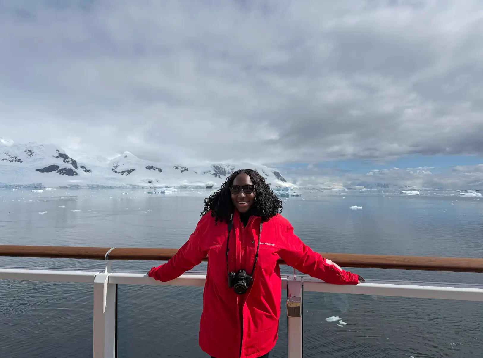 The writer wearing a red jacket and standing in front of ice-covered mountains on a cruise in Antarctica.