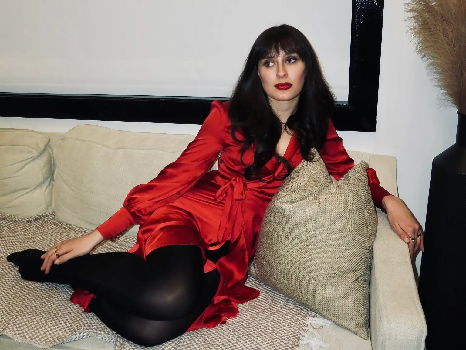 a woman poses in a red dress on a couch