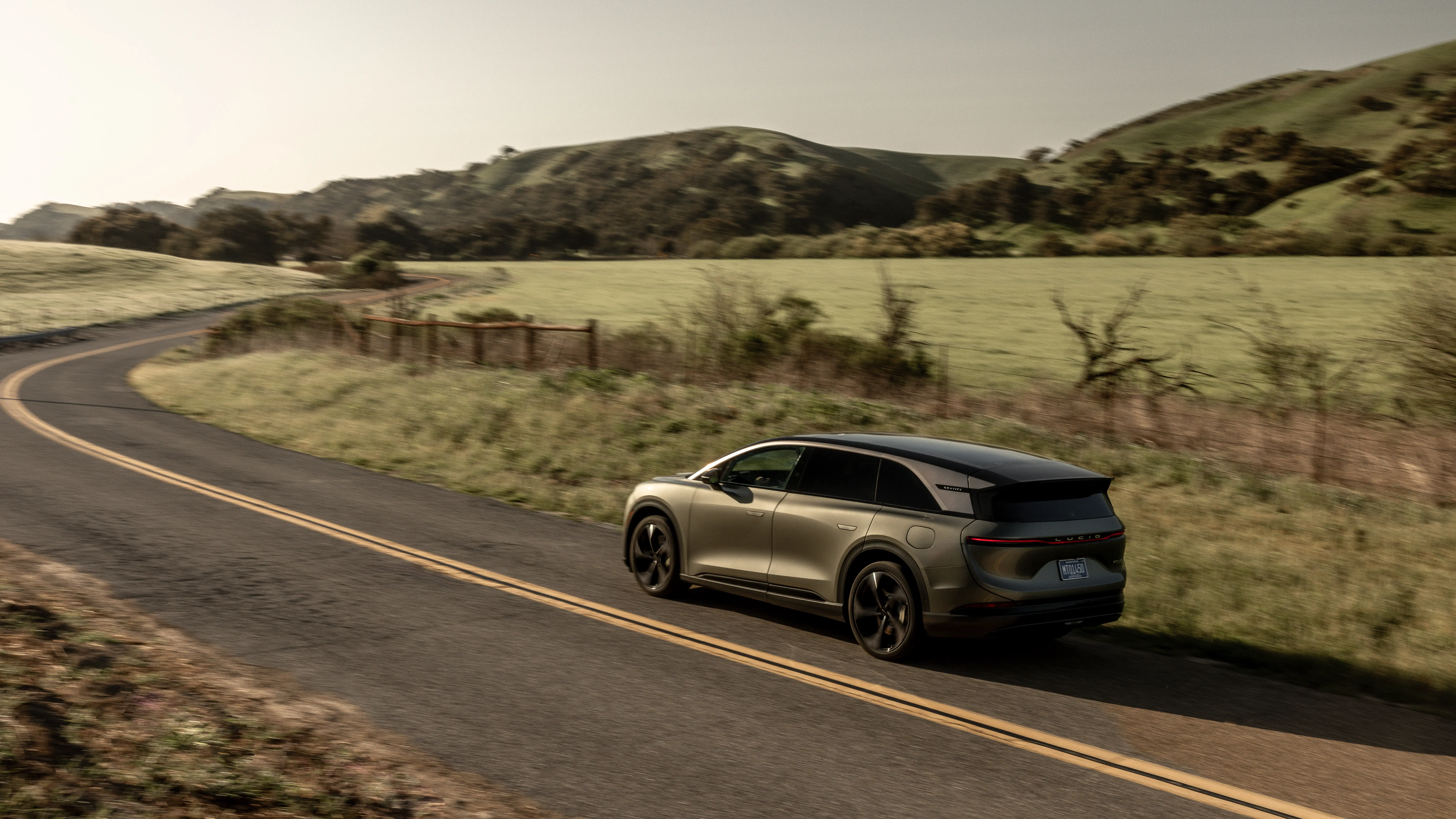 A Lucid Gravity SUV drives down a two-lane road.