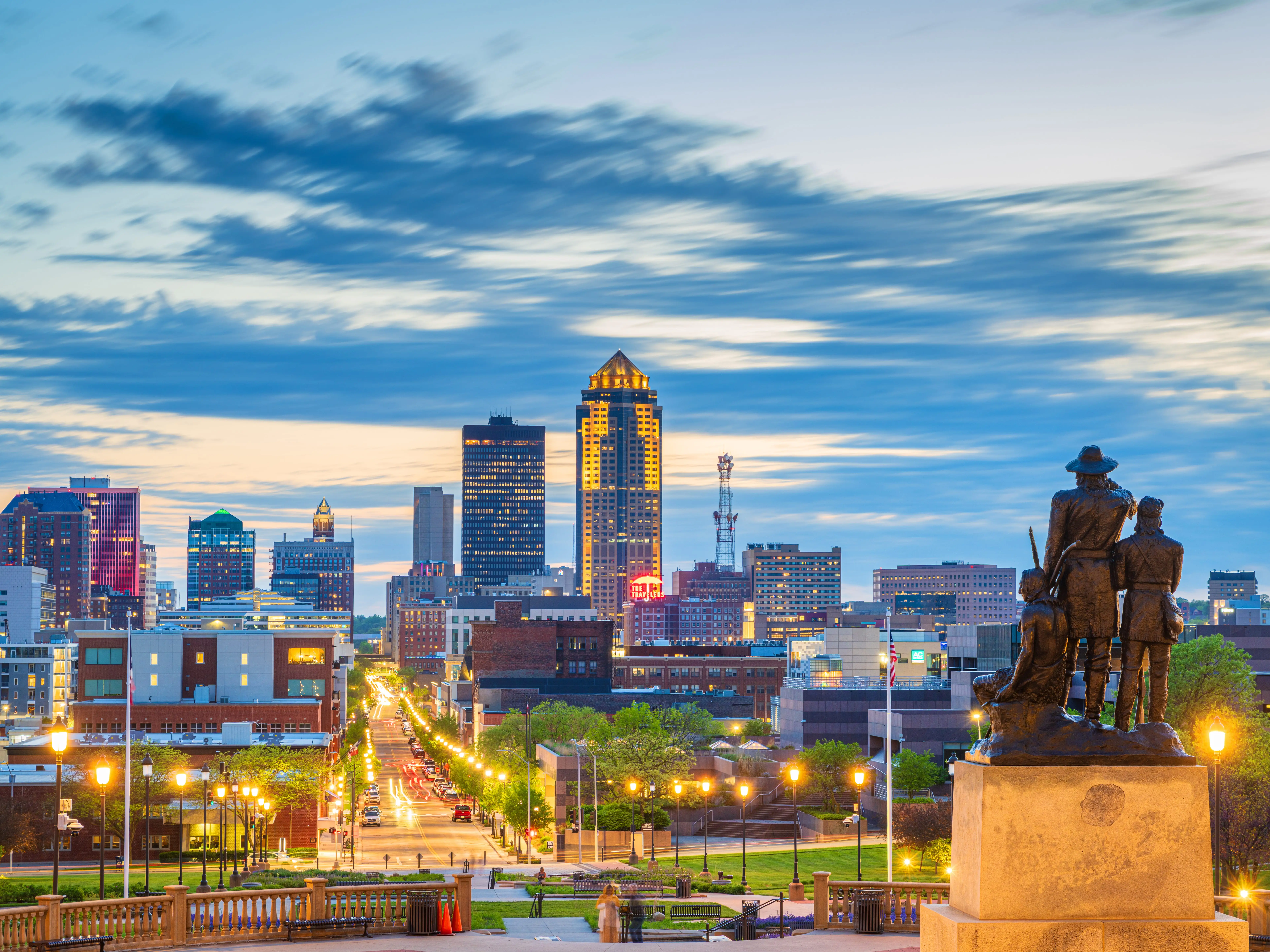 DES MOINES, IOWA, USA - MAY 3, 2024: The Pioneer Statuary Group on the Iowa State Capitol grounds with the Des Moines skyline in the distance at dusk.