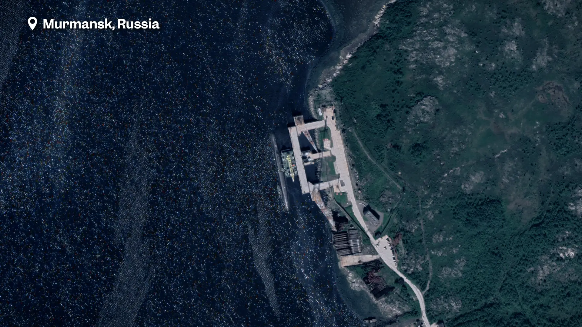 A satellite image of a dock with a submarine in the water. The image is labelled Murmansk, Russia.