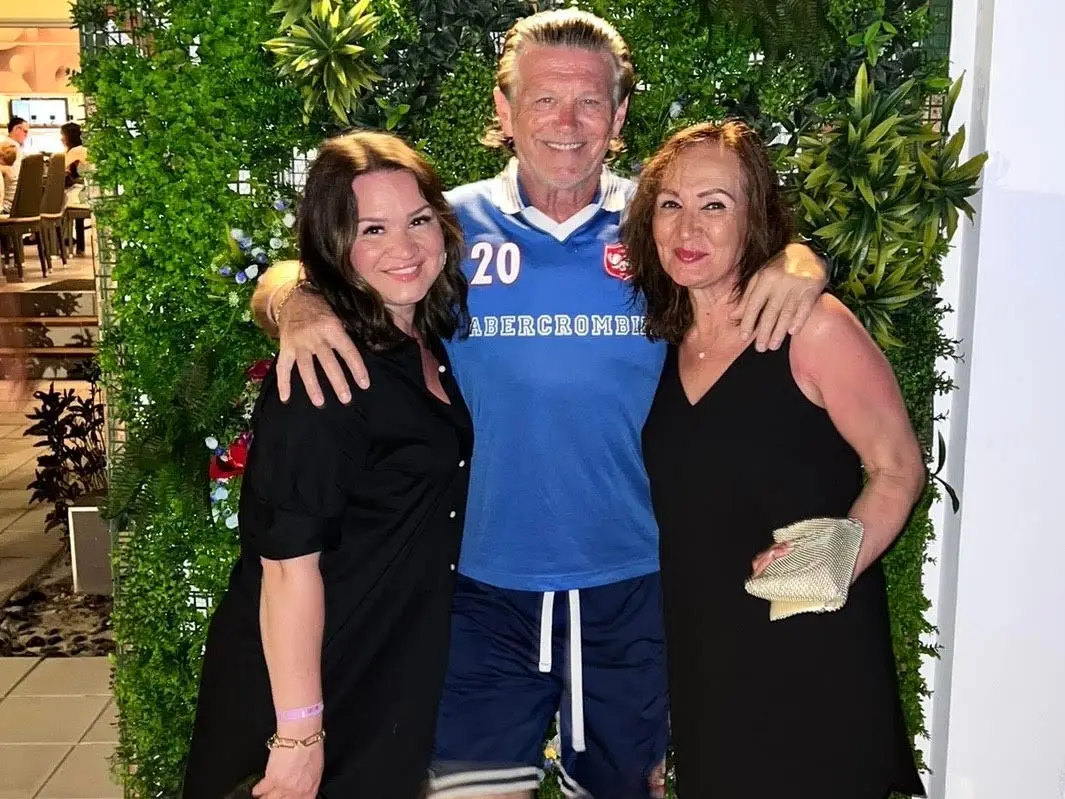 A woman poses for a photo in front of greenery with her parents.