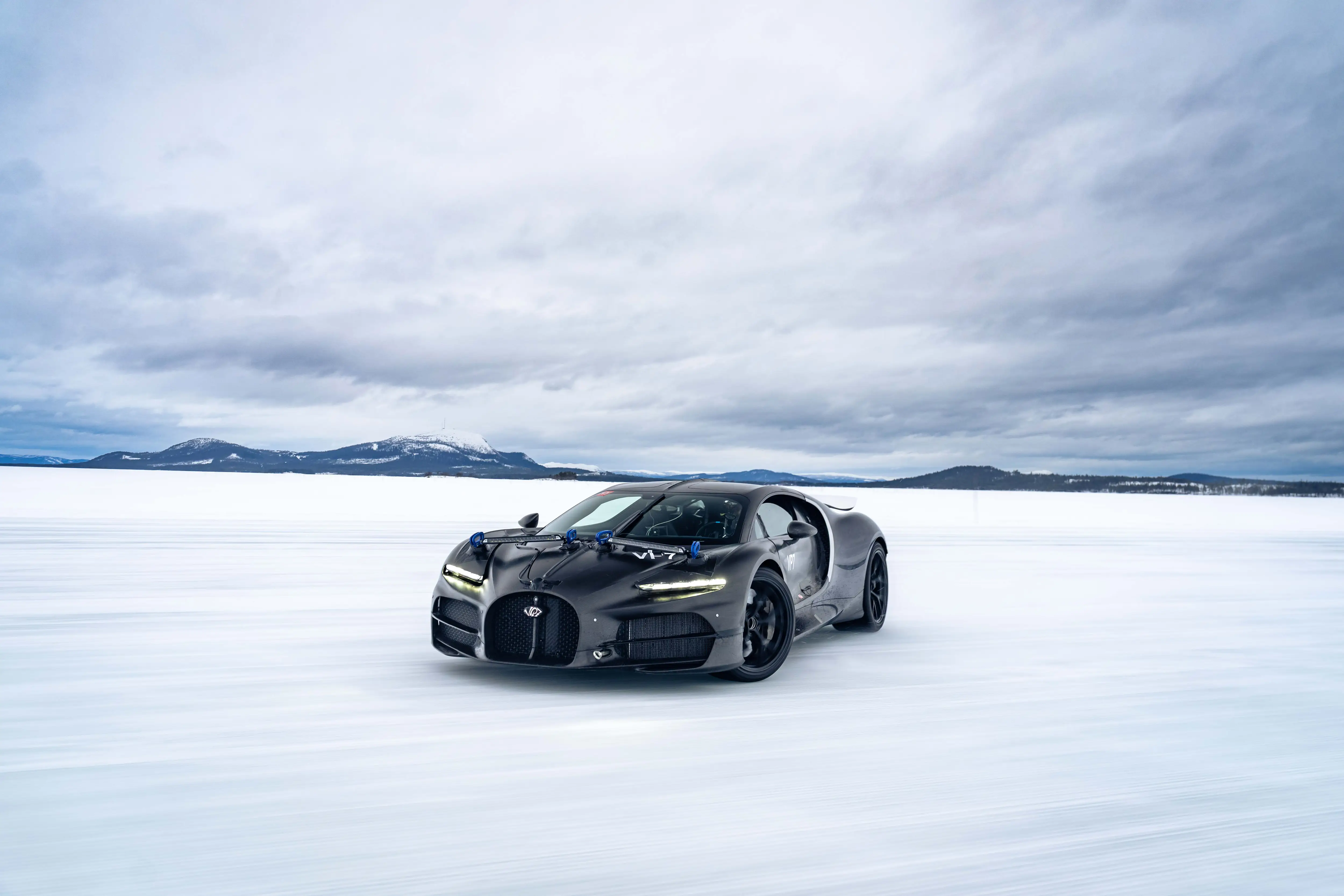 A black Bugatti Tourbillon drives on a snowy track.