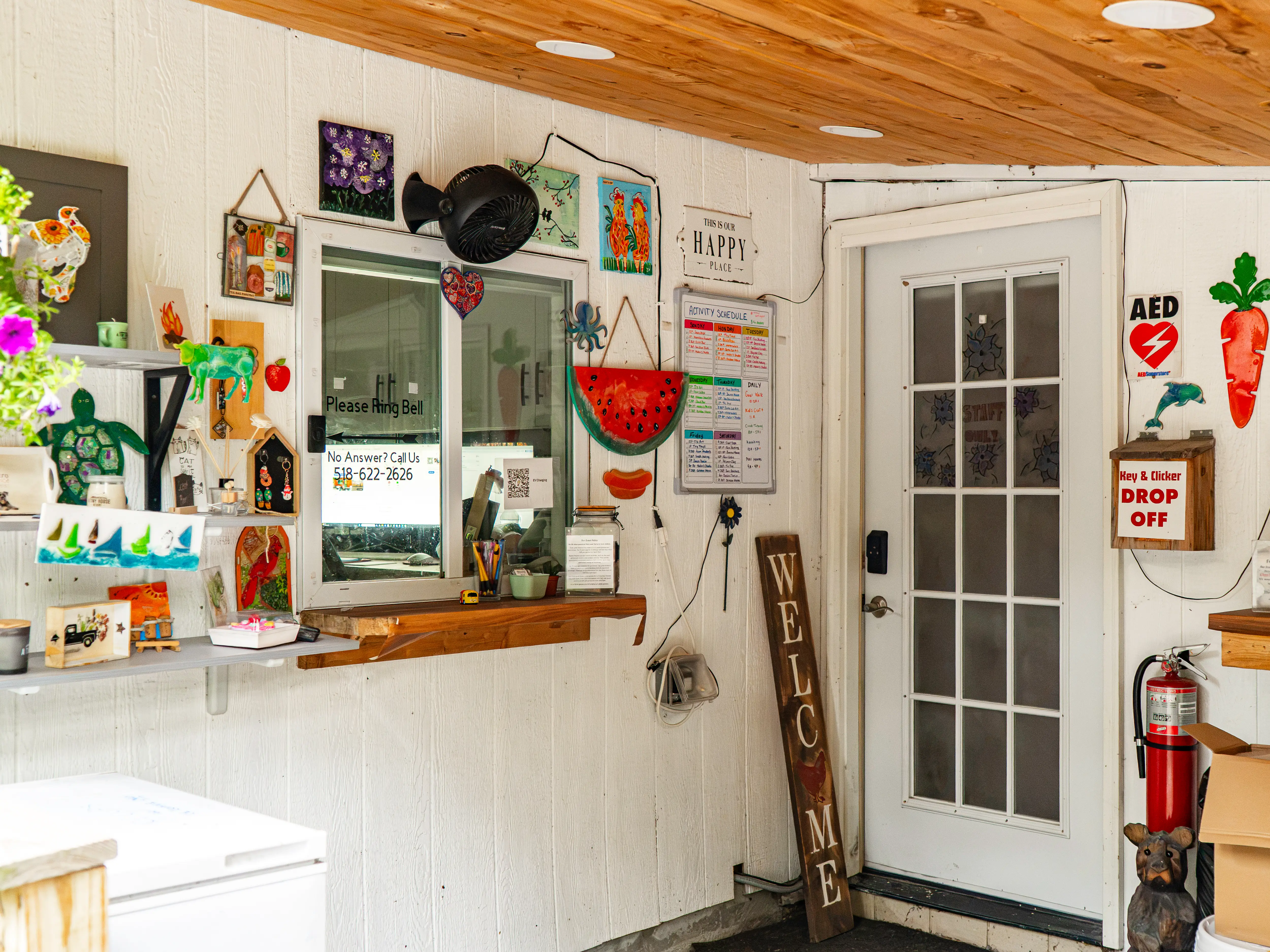 Decorated reception area with service window, white glass door, AED sign, fire extinguisher, and vertical WELCOME sign.