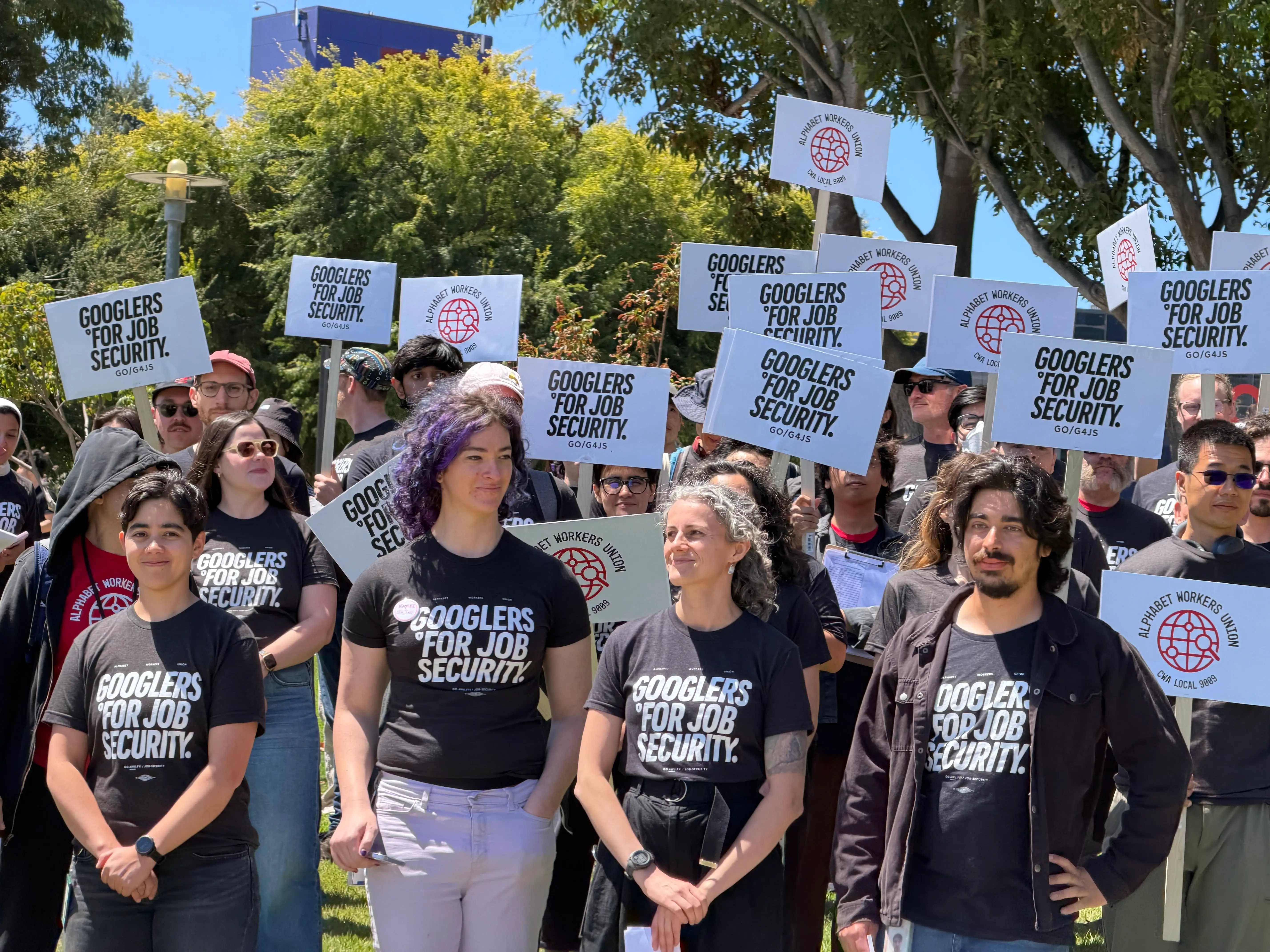 Crowd outdoors holds signs and wears shirts reading