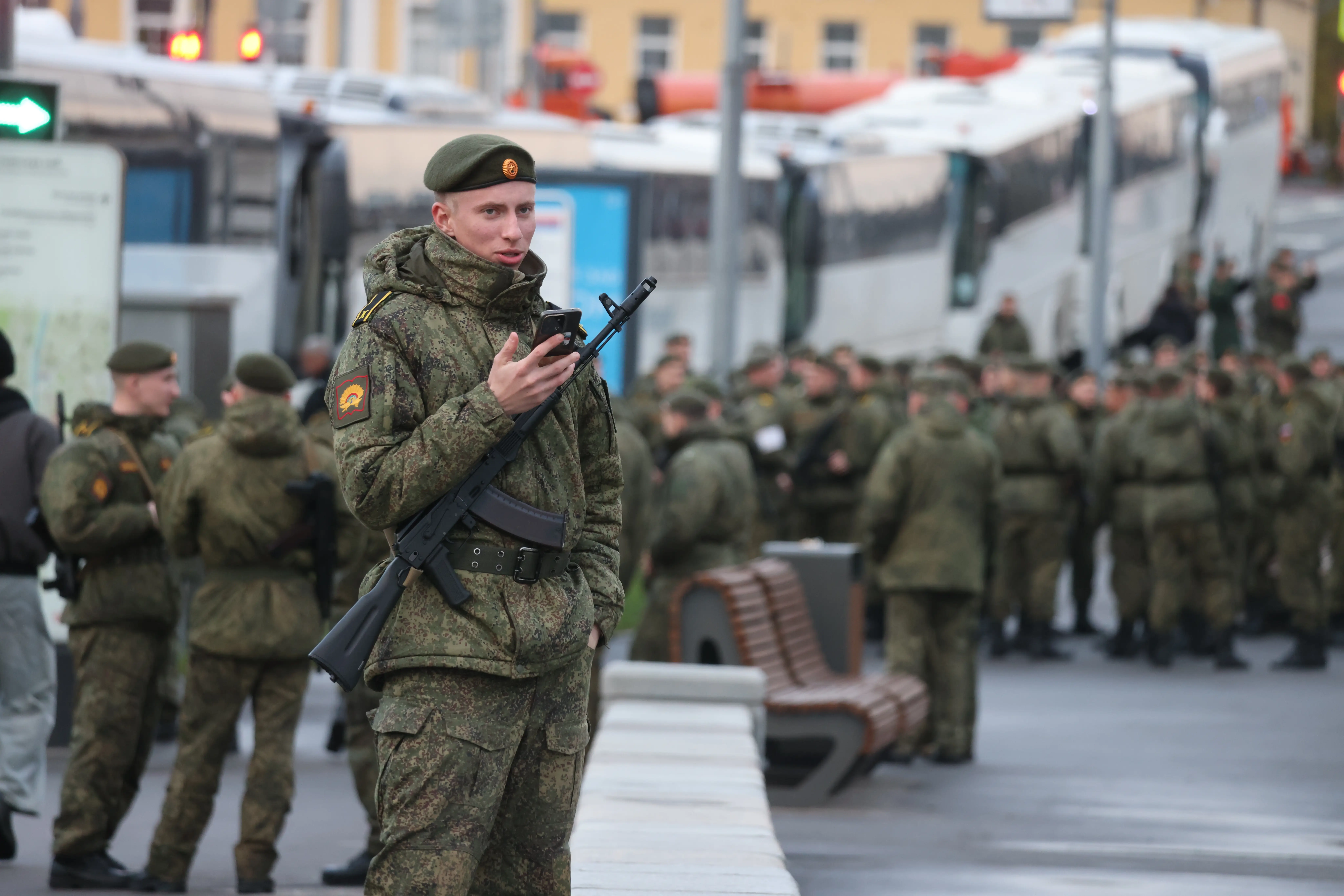 A Russian military cadet holds a cellphone as he waits near a fleet of buses.