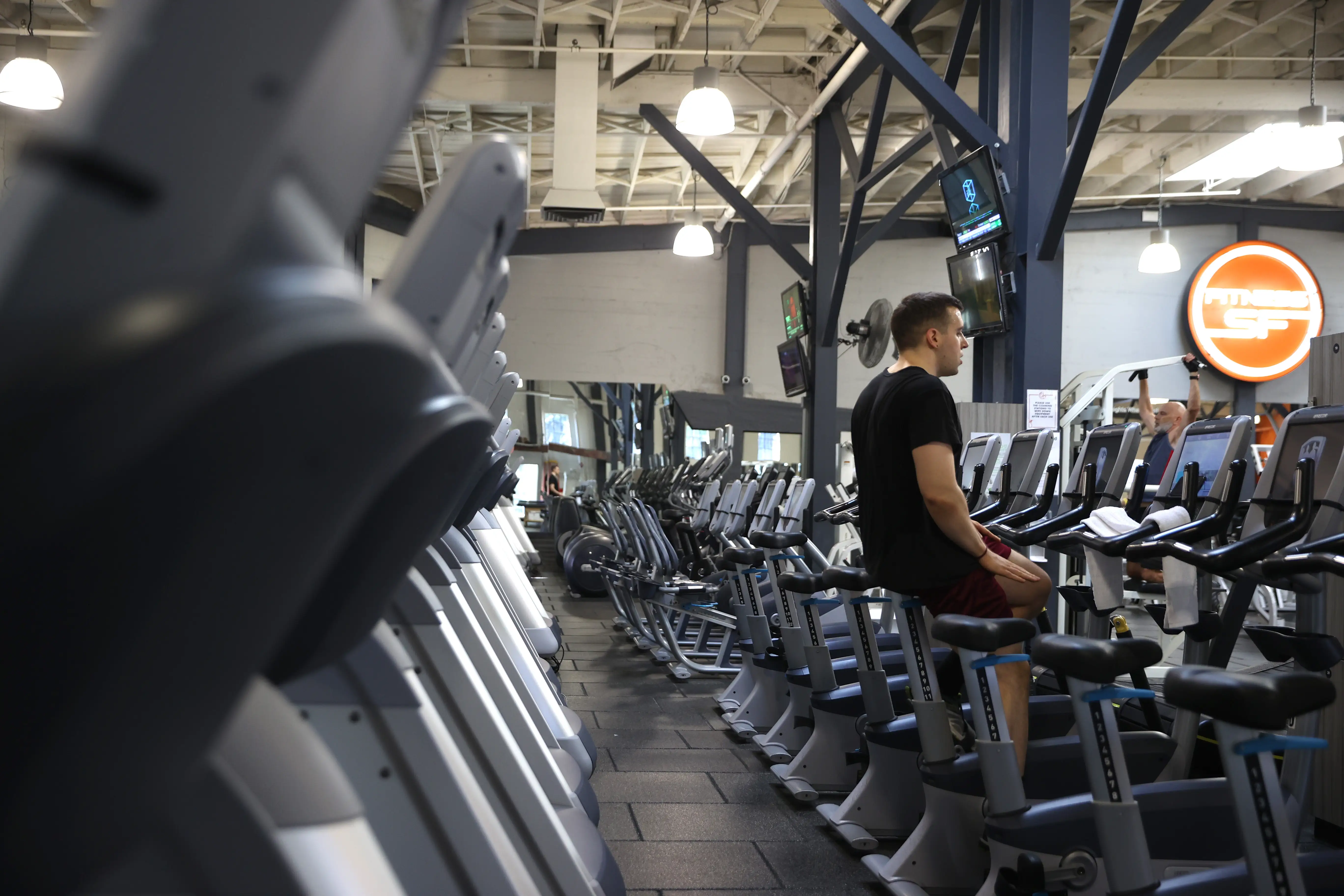 Rows of cardio machines fill a gym while a person sits on a stationary bike.