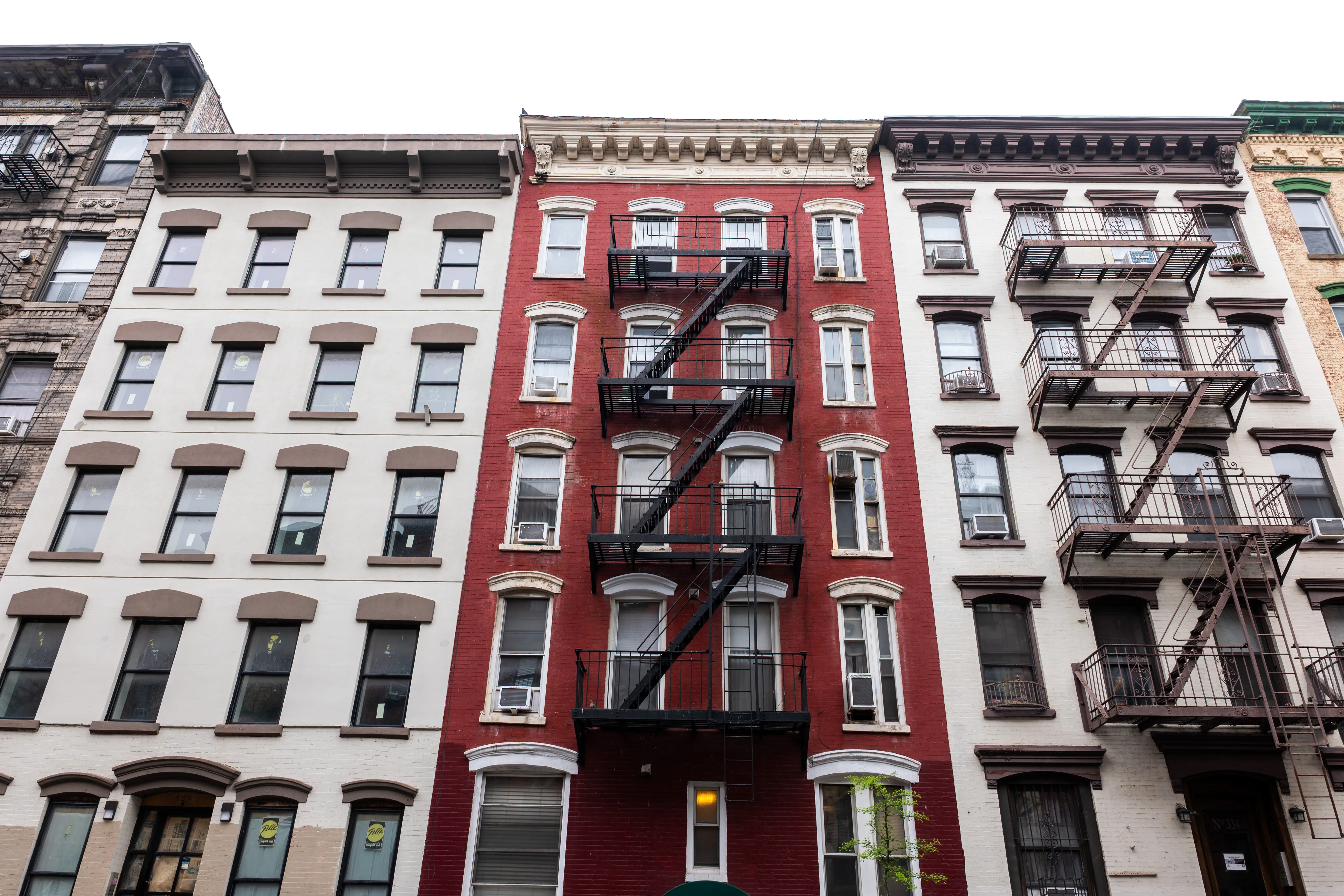 Historic multi-story apartment building facades with black metal fire escapes line an urban street.