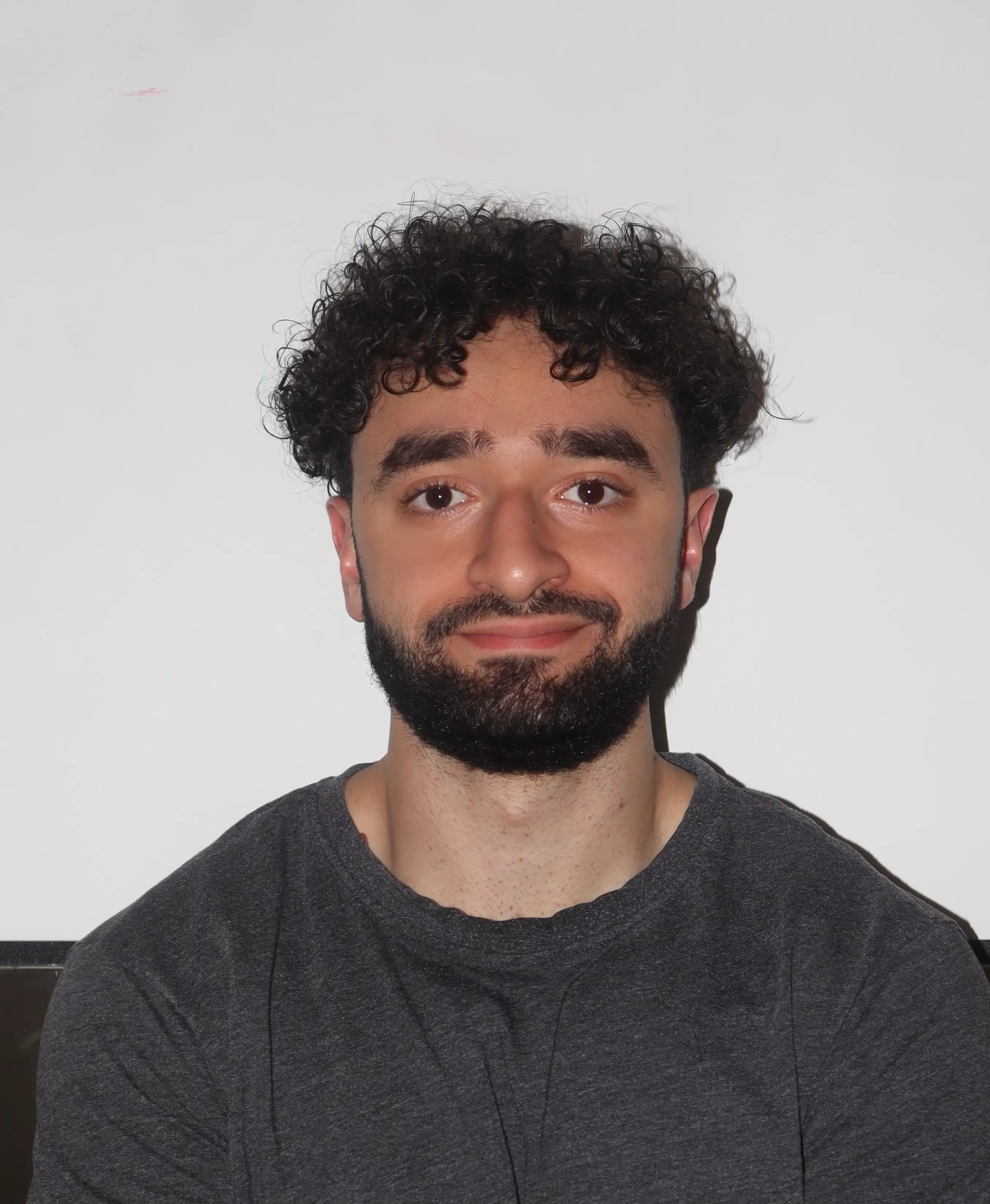 Hamza Mostafa is in front of a white background wearing a grey t-shirt.