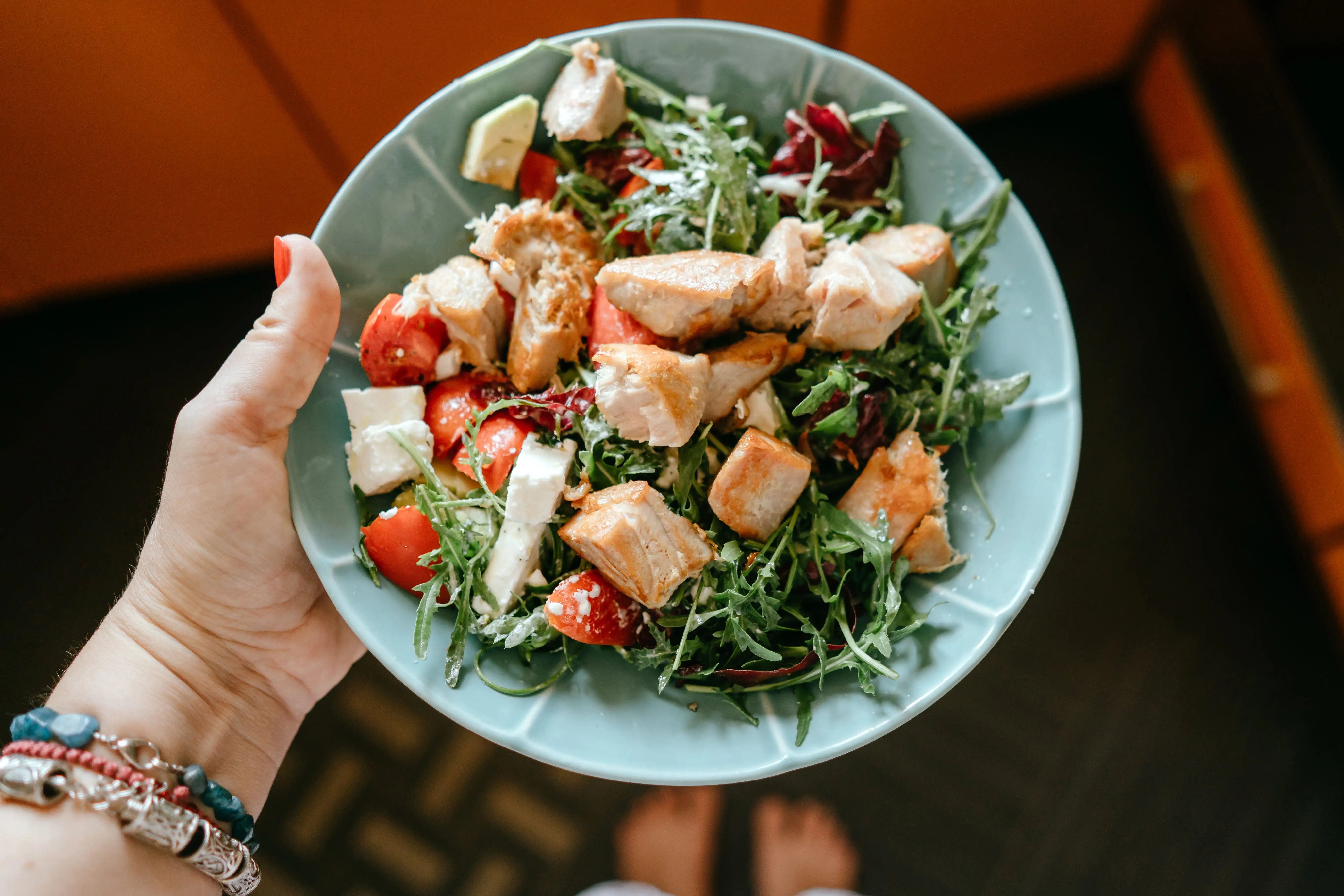 Hand holding salad with chicken, arugula, tomatoes