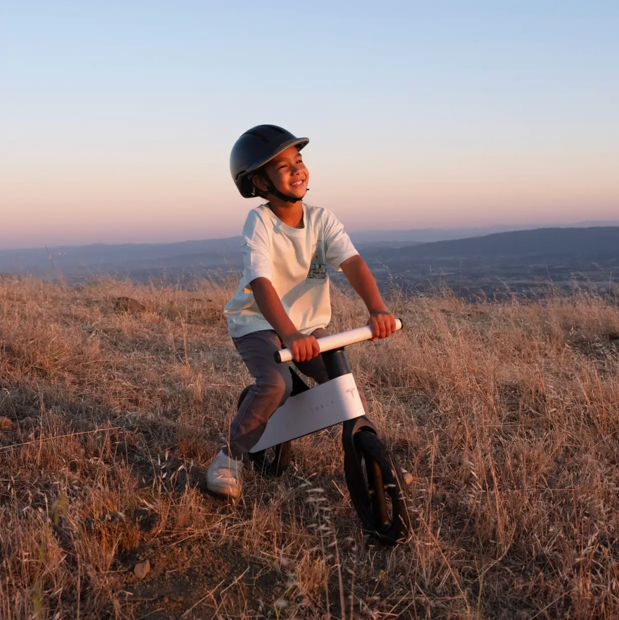 A child in a field rides a Tesla bike.