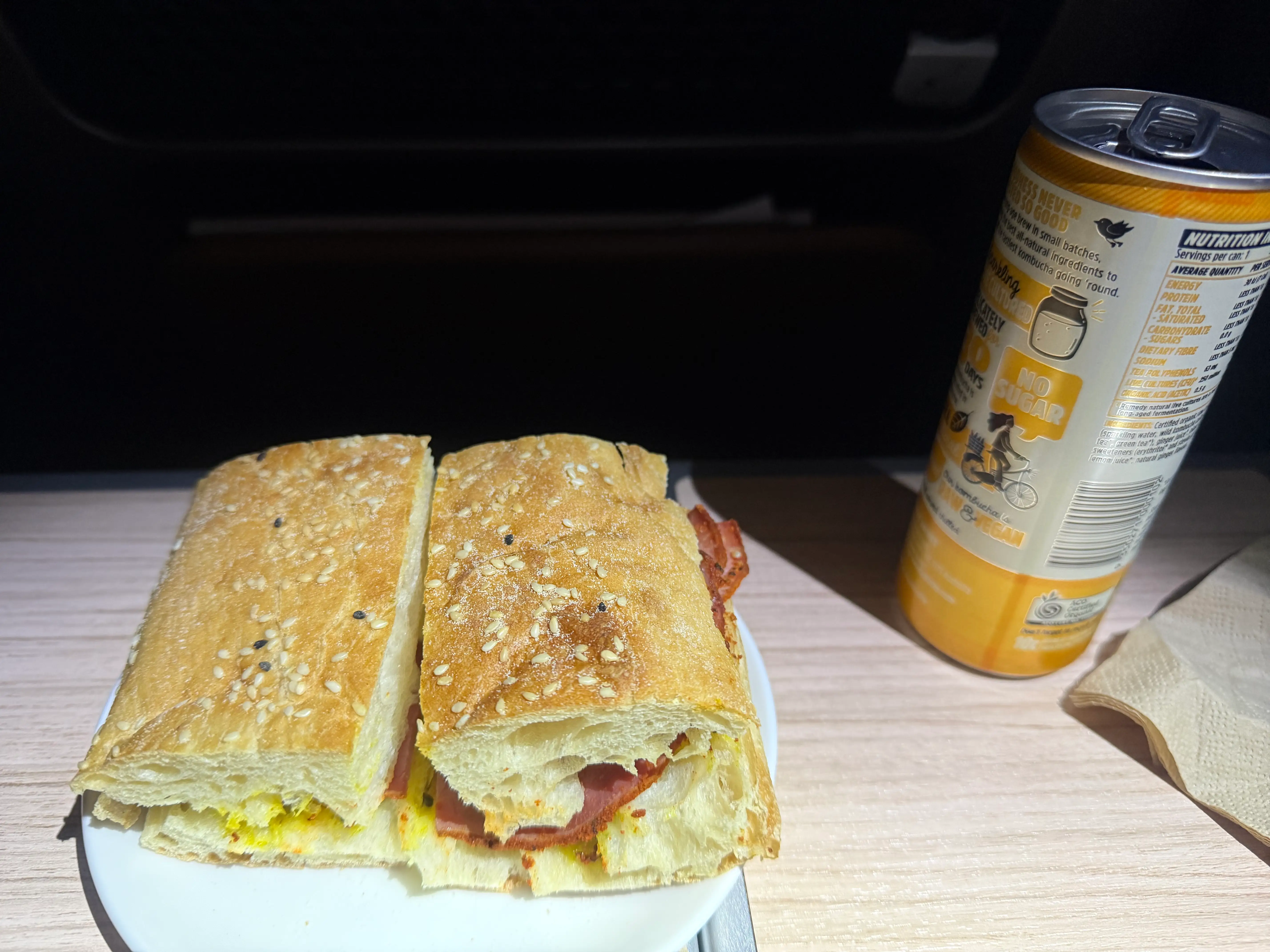 Pastrami and cheese sandwich and canned drink on tray table on  Qantas premium flight