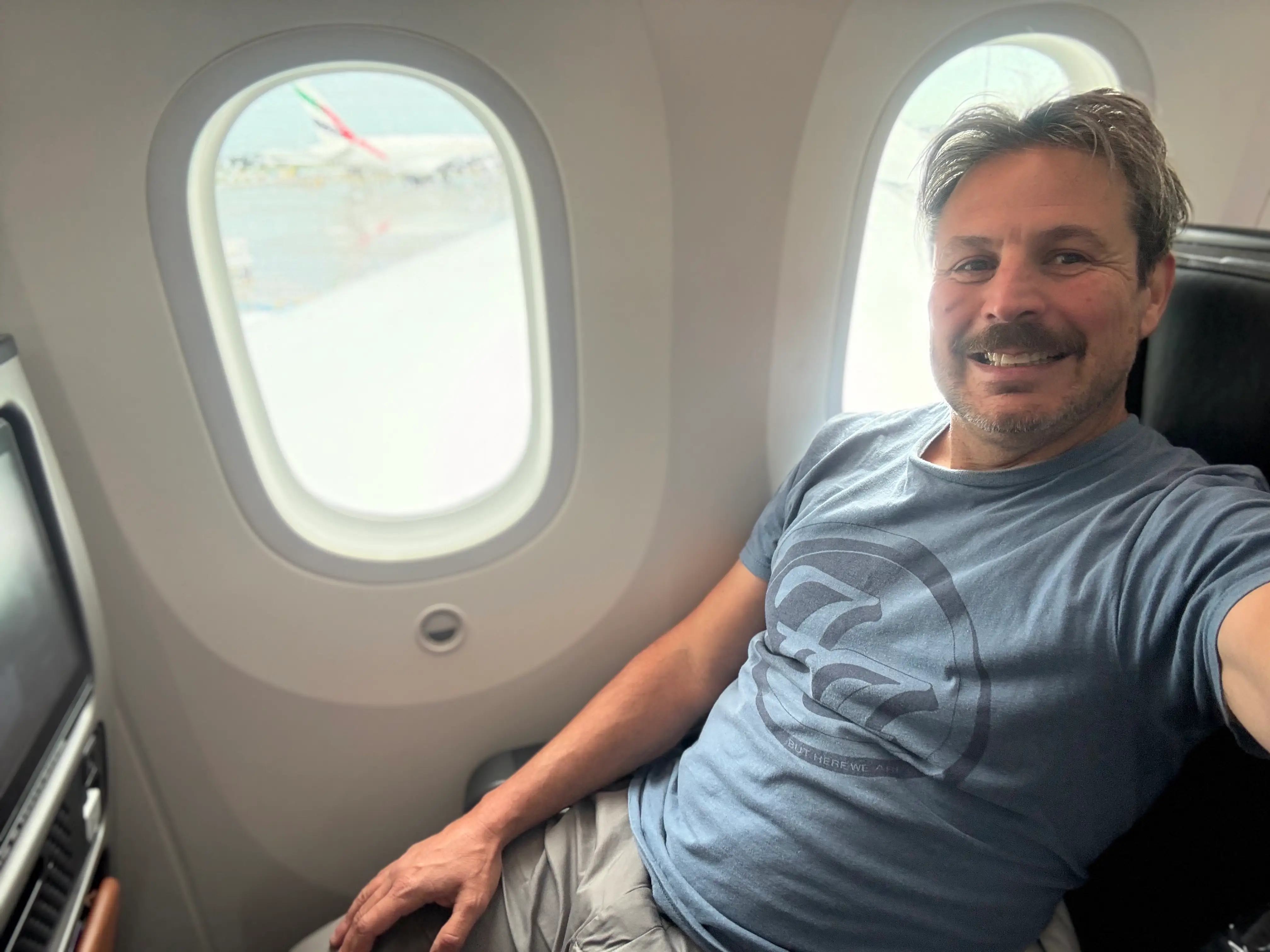 Author Ash Jurberg in premium economy seat next to window, smilnig