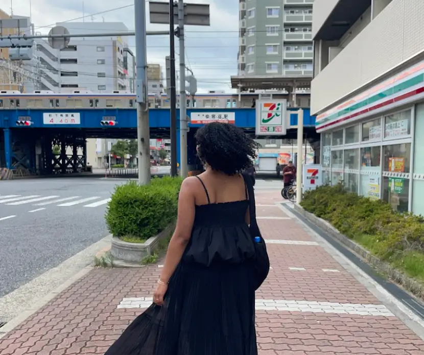 The writer, wearing a black dress, faces away from the camera with a 7-11 in the background.