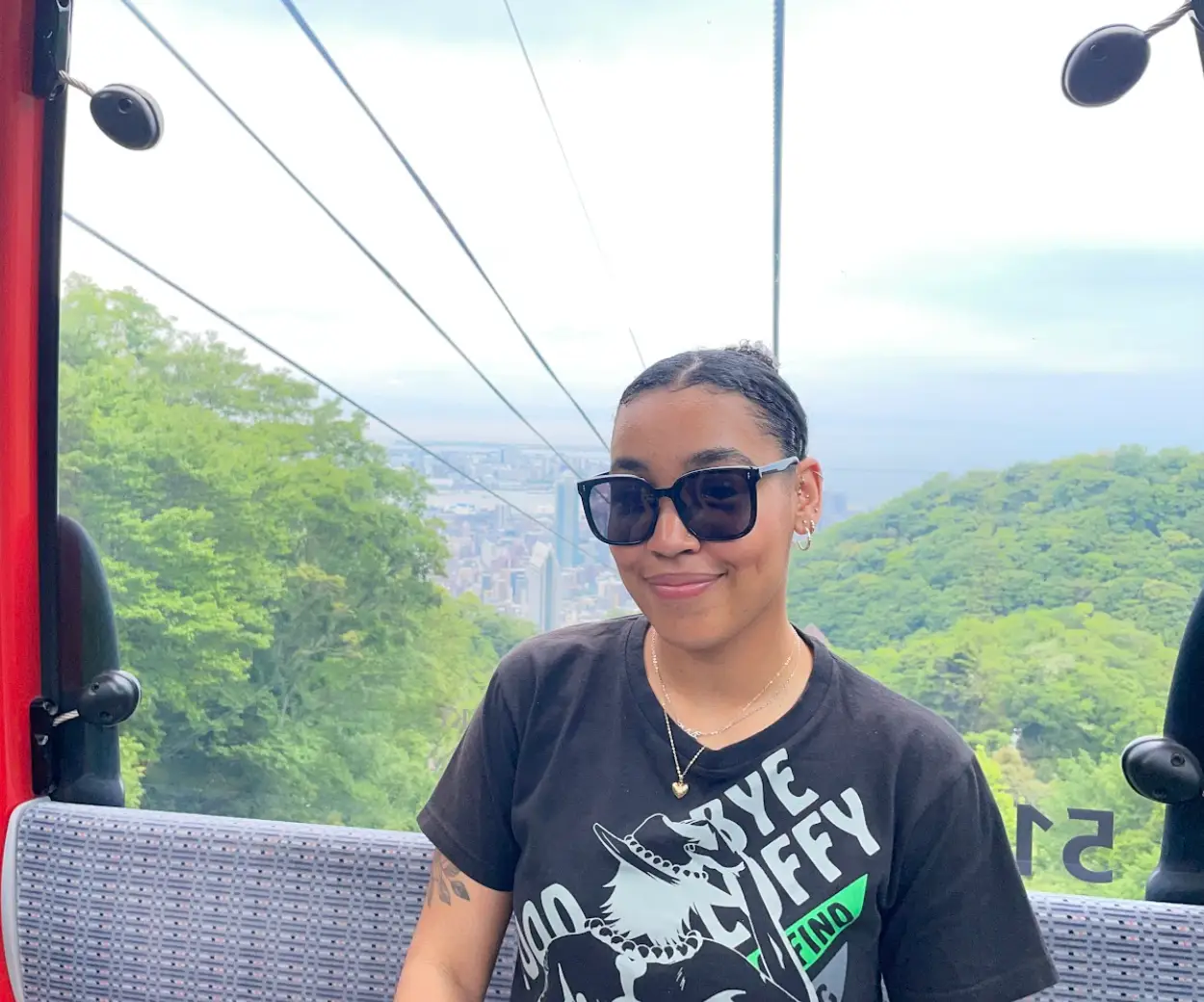 The writer wearing sunglasses, sitting in a cable car above green hills with a distant city view.