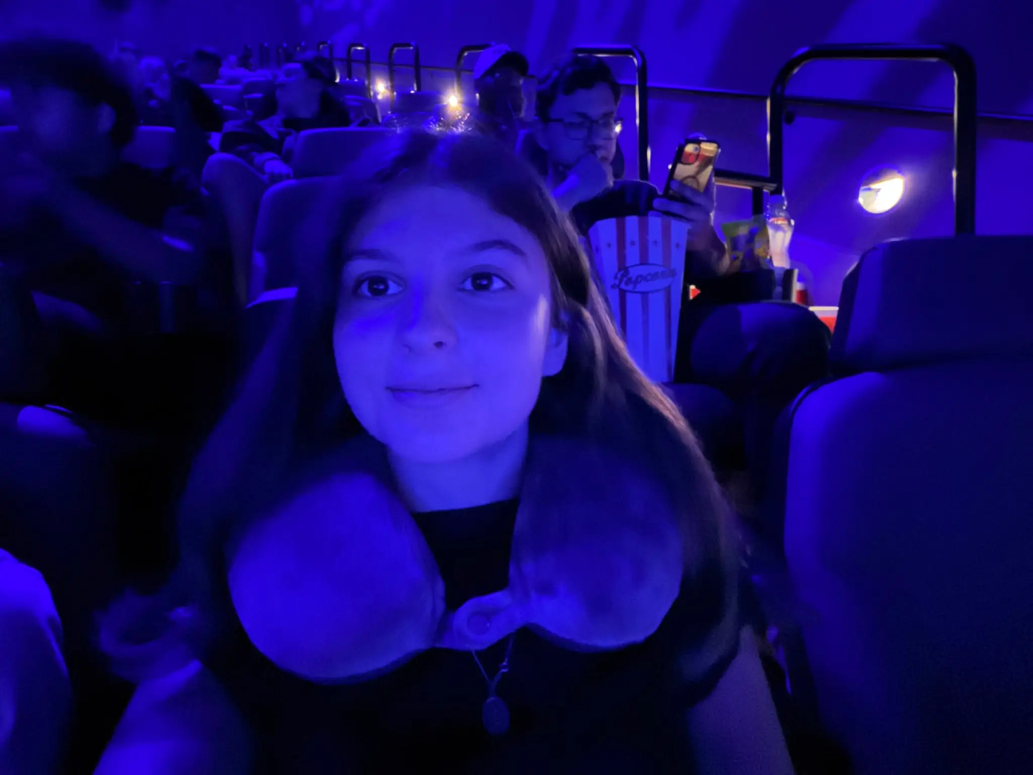 A girl sits in a cinema with a neck pillow