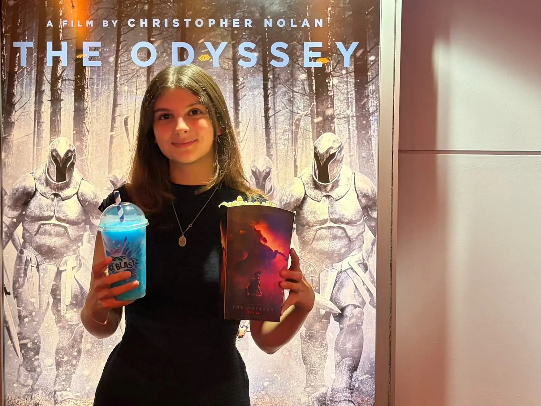 a girl stands in front of The Odyssey poster